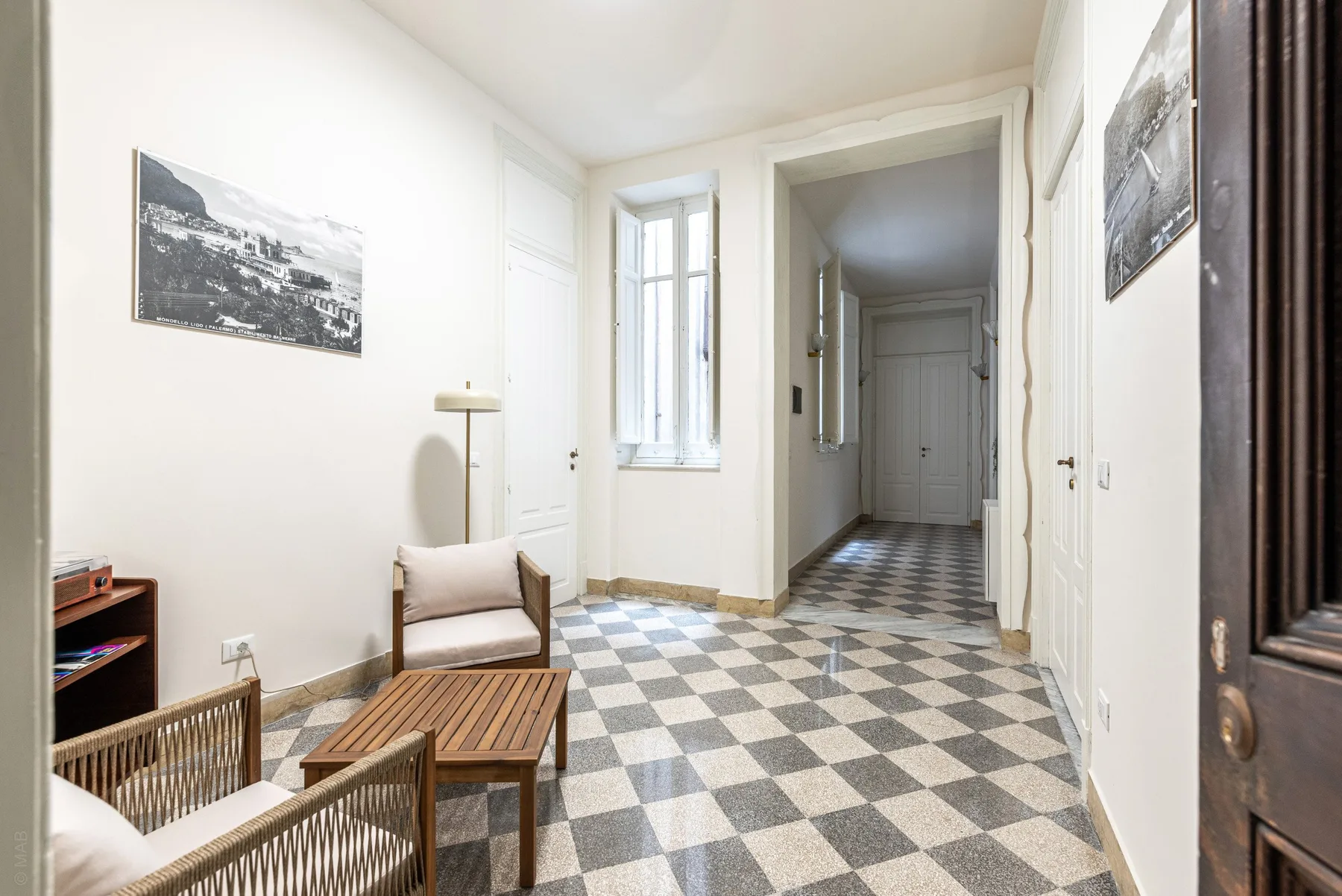 A bright hallway with a checkered floor and a small seating area.