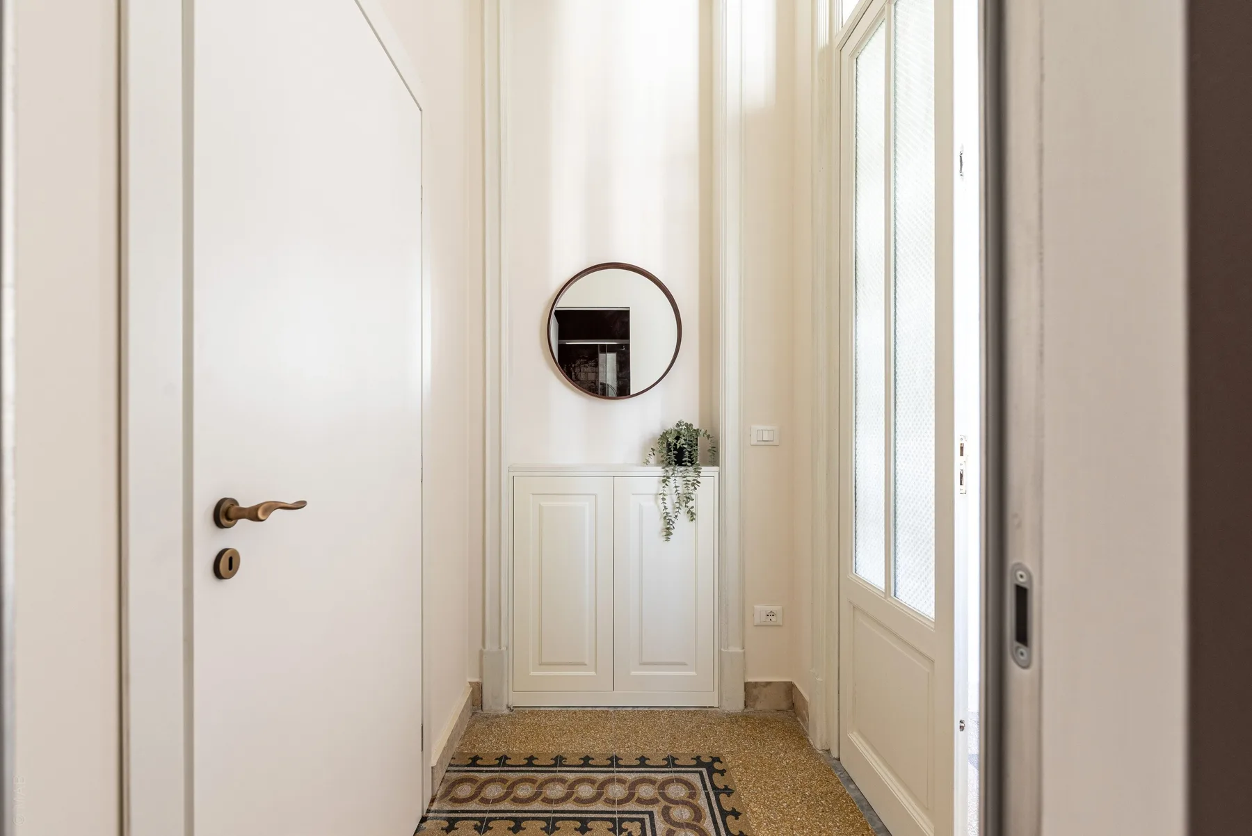 A bright entry hall with a patterned rug and a small cabinet beneath a round mirror.
