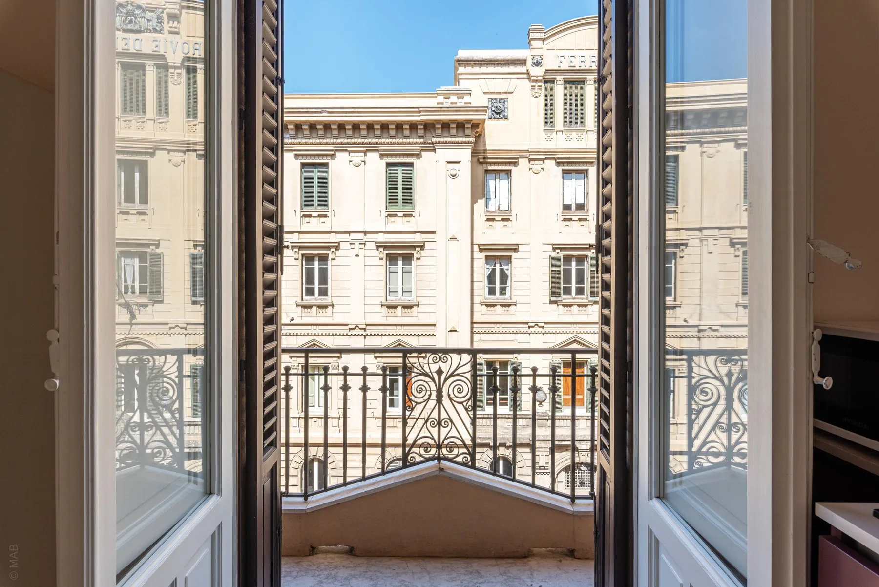 An open window looks out onto an ornate balcony and a neighboring building.