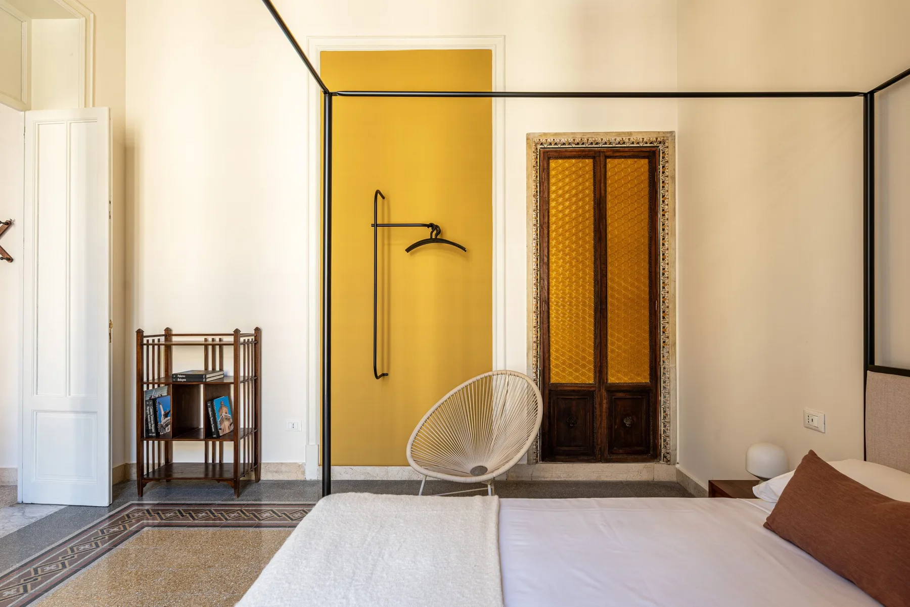 A bedroom with a bed, a woven chair, and a yellow wall.