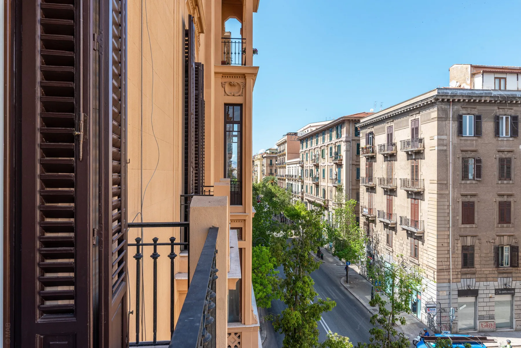 A city street lined with multi-story buildings is viewed from a balcony.