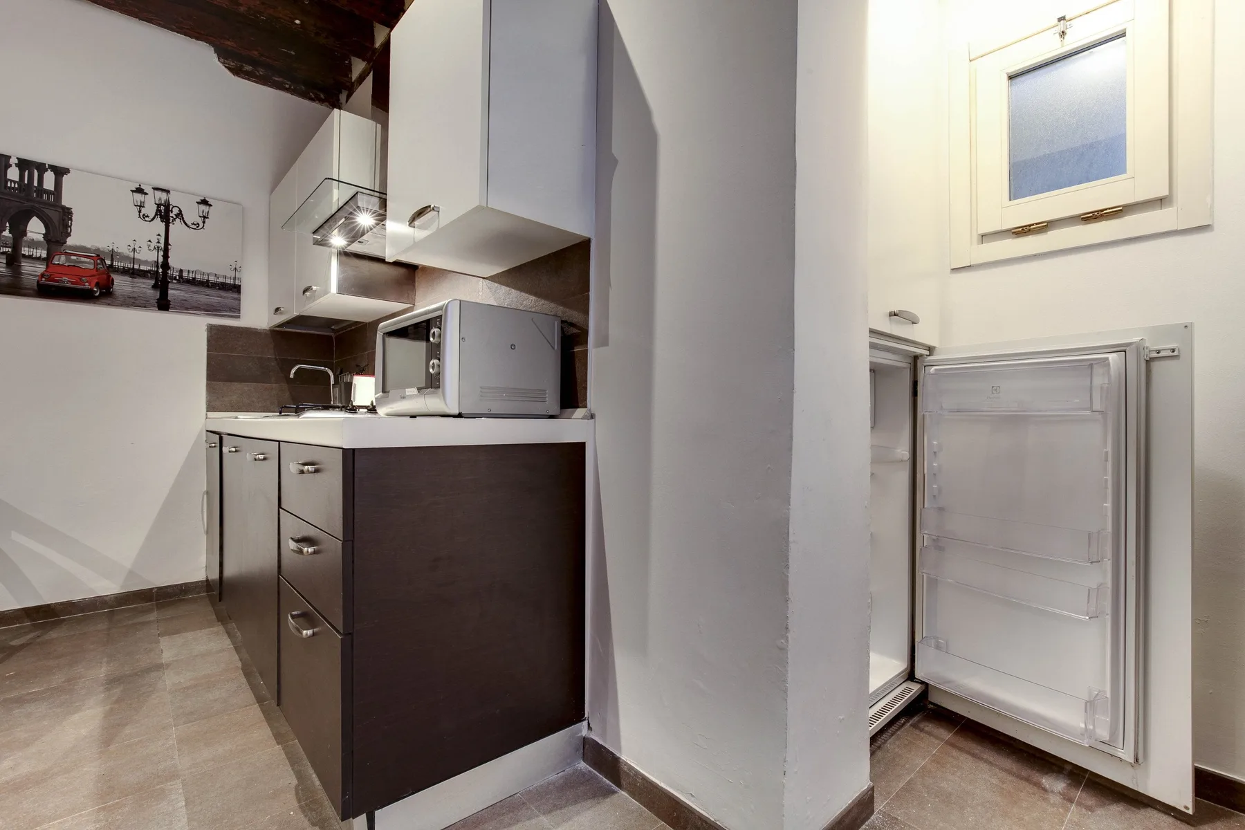 A compact kitchen with dark cabinetry and a refrigerator.