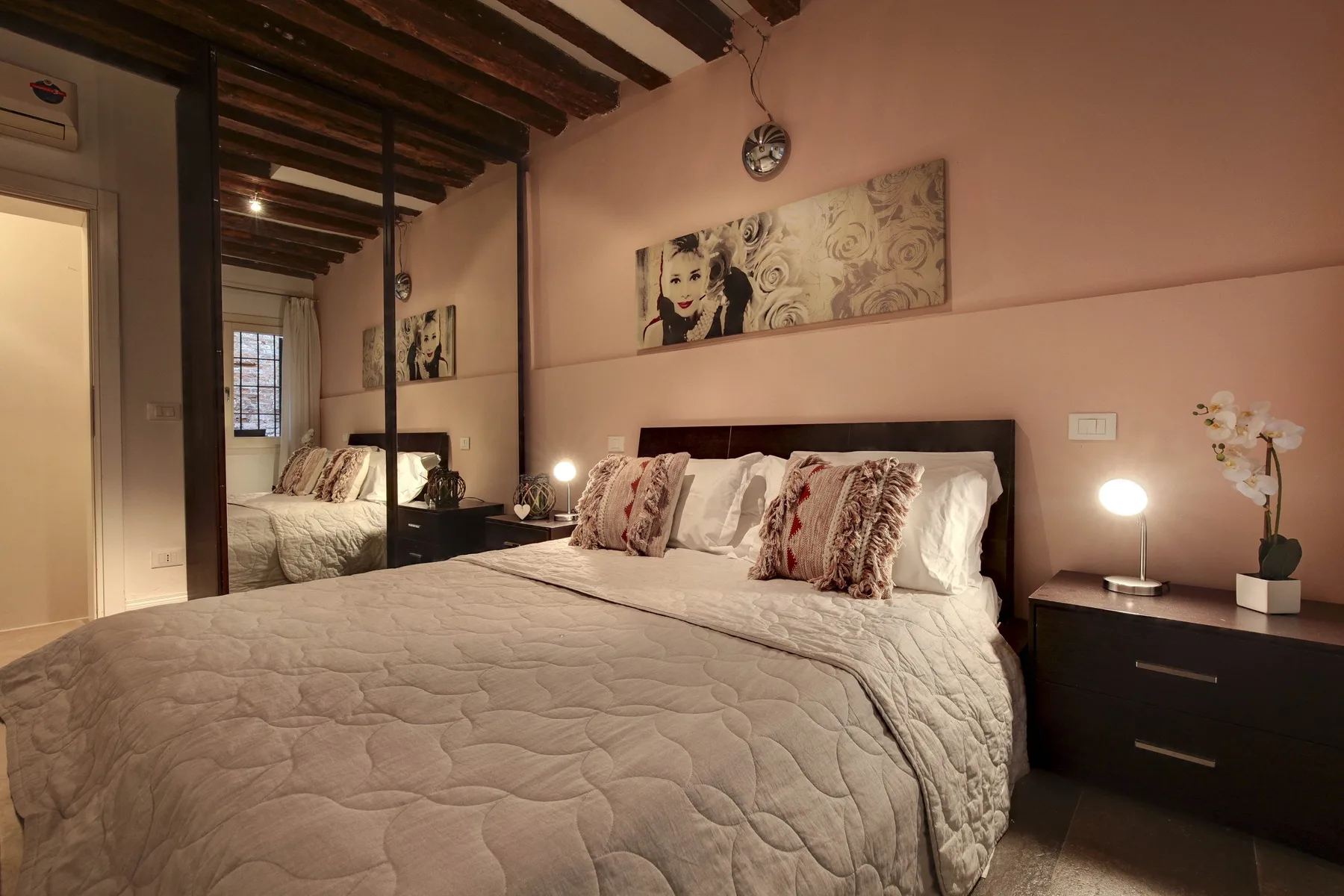 A bedroom with a large bed, patterned pillows, and a mirrored wall.