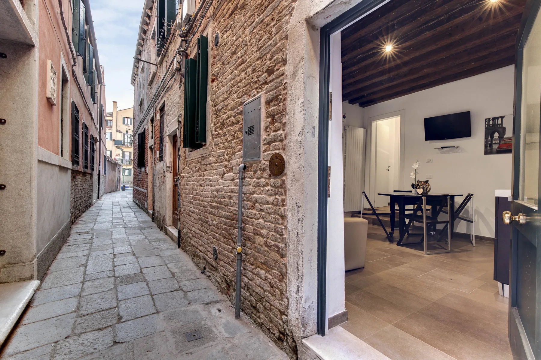 Un callejón estrecho pavimentado con piedra junto a una puerta abierta que da a un comedor.