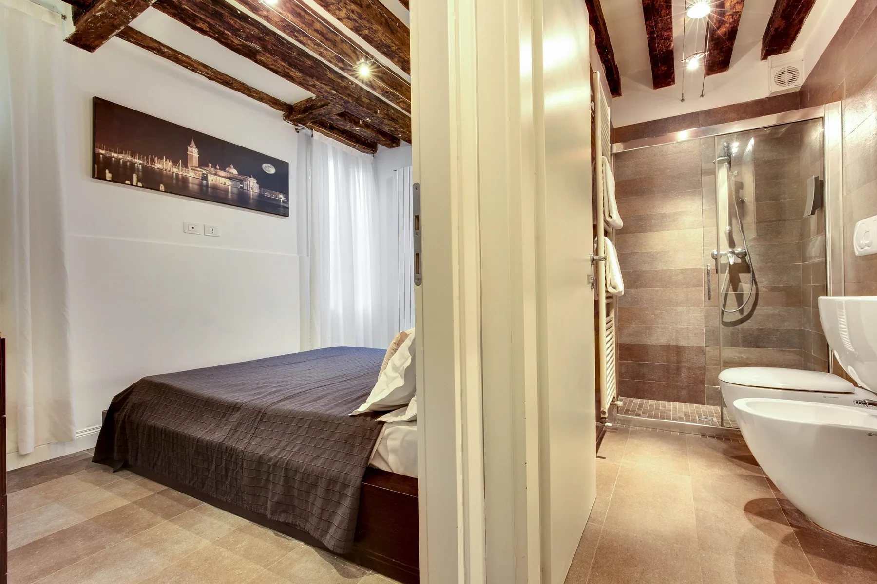 A bedroom with a bed sits beside a bathroom with a shower.