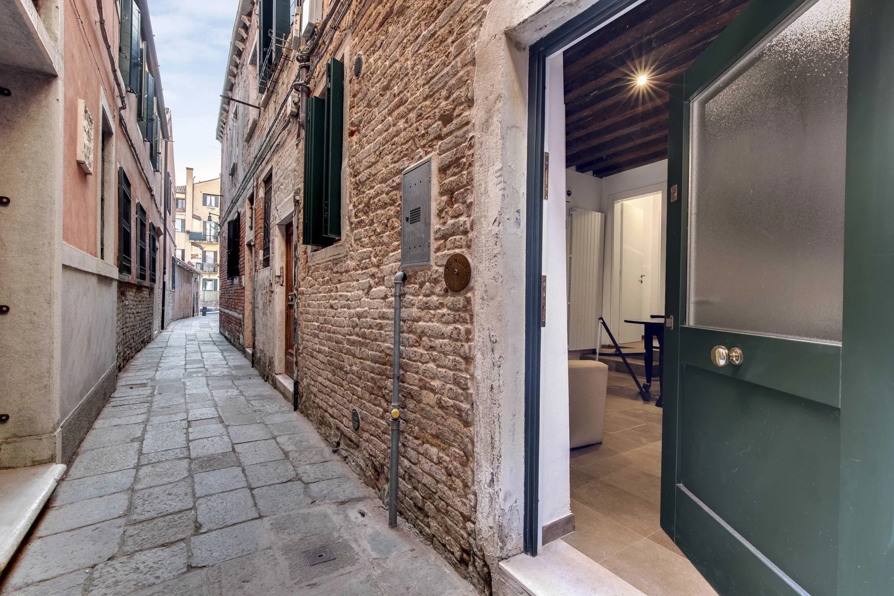 A narrow stone-paved alley leads past an open doorway into an interior.
