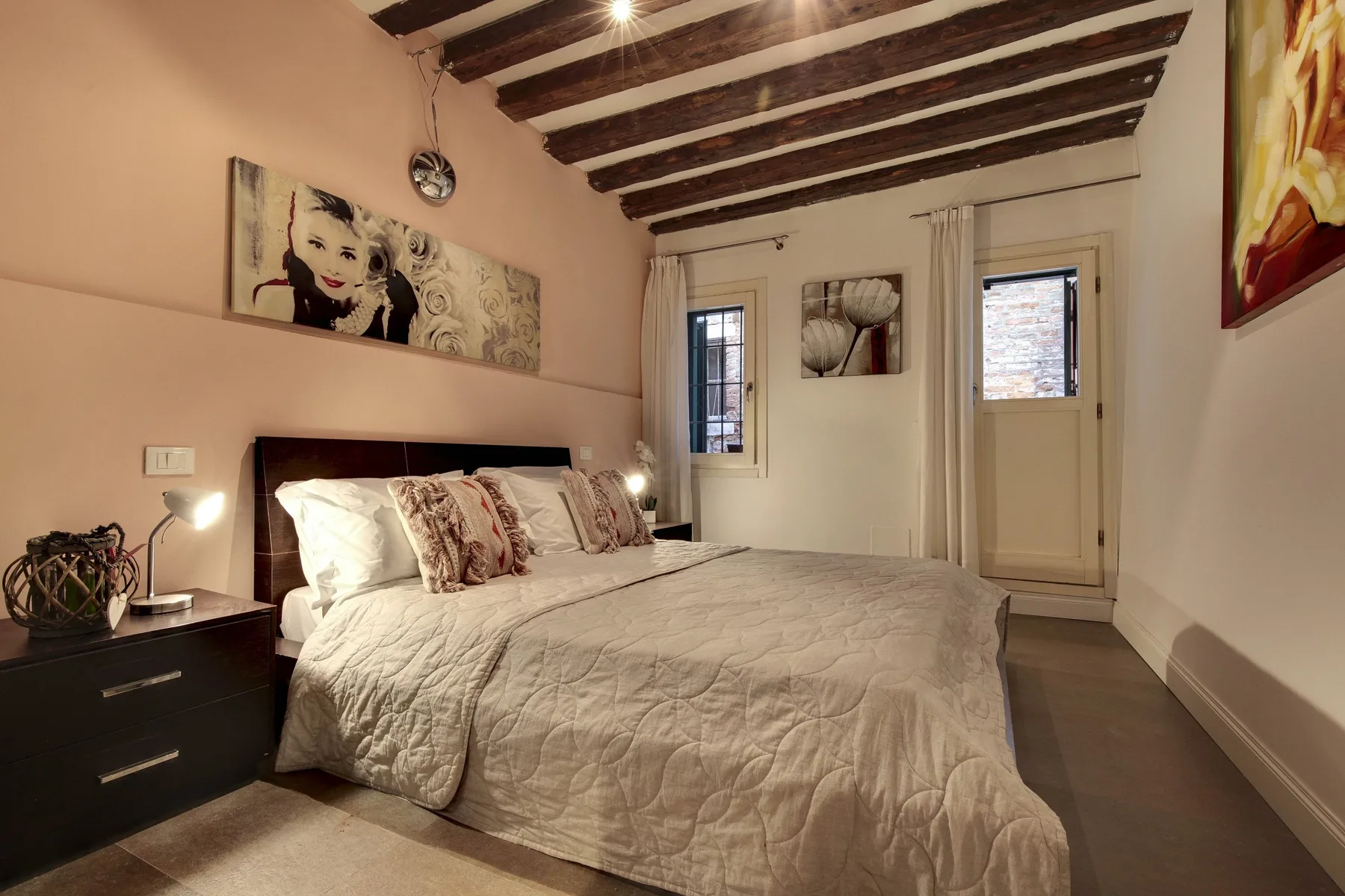 A bedroom with a large bed beneath exposed dark ceiling beams.