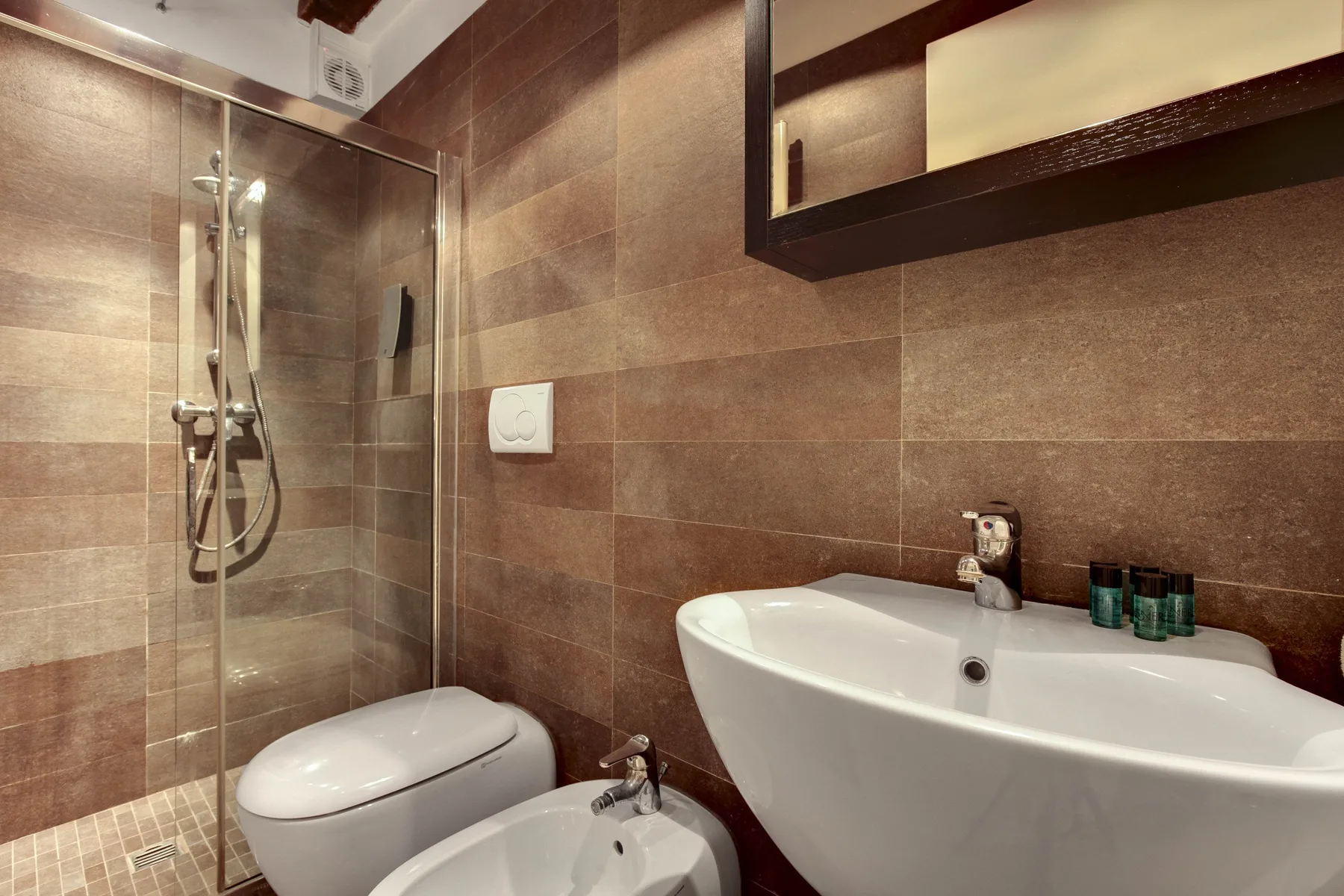 A tiled bathroom with a glass shower, toilet, and bathtub.