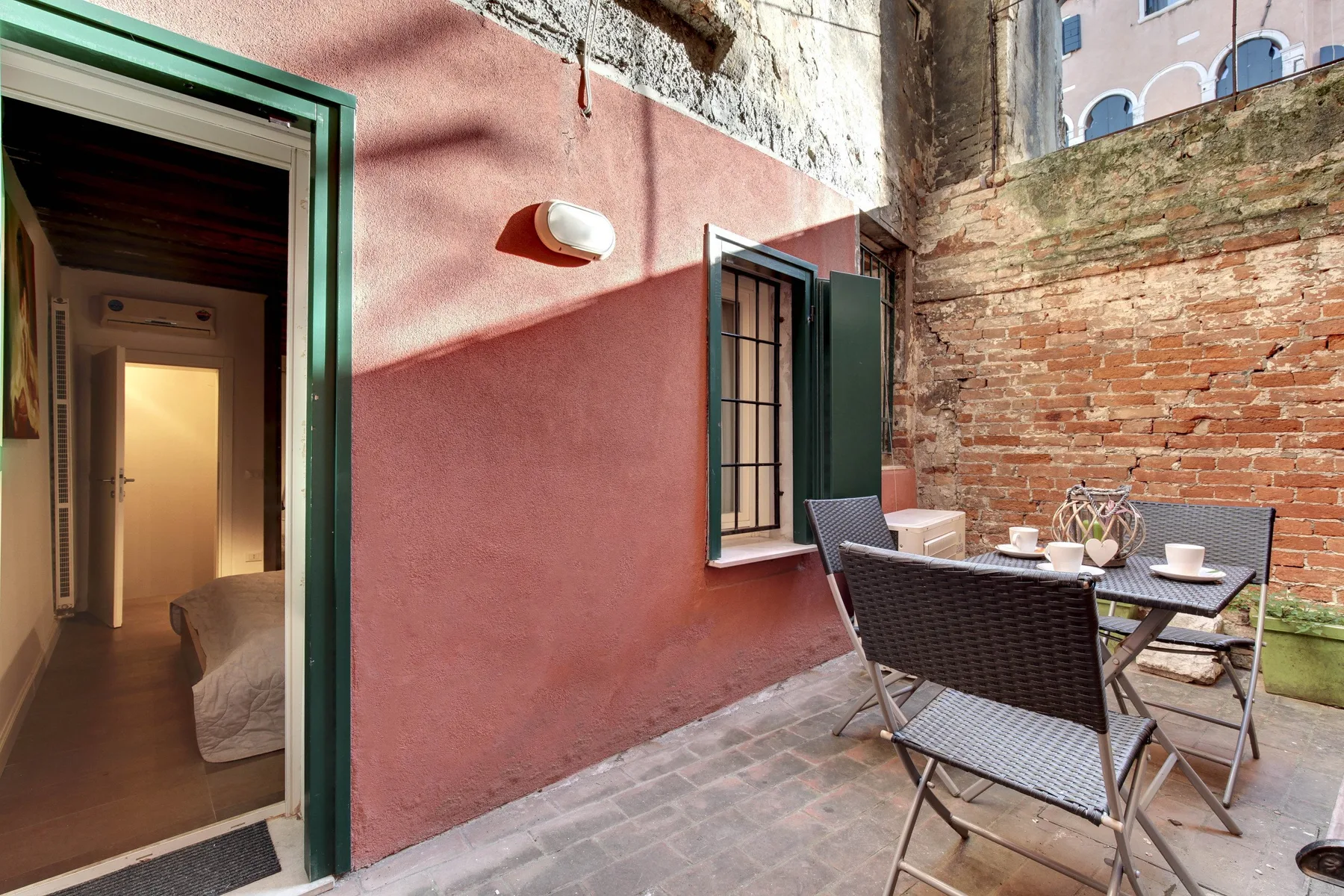 Un pequeño patio exterior con una mesa y sillas junto a una pared rosa.