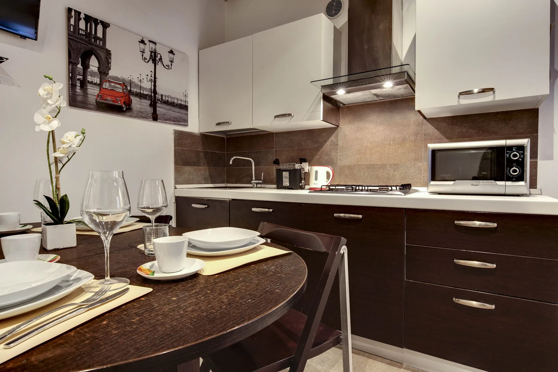 A dining area beside a modern kitchen, with a set table and white cabinets.