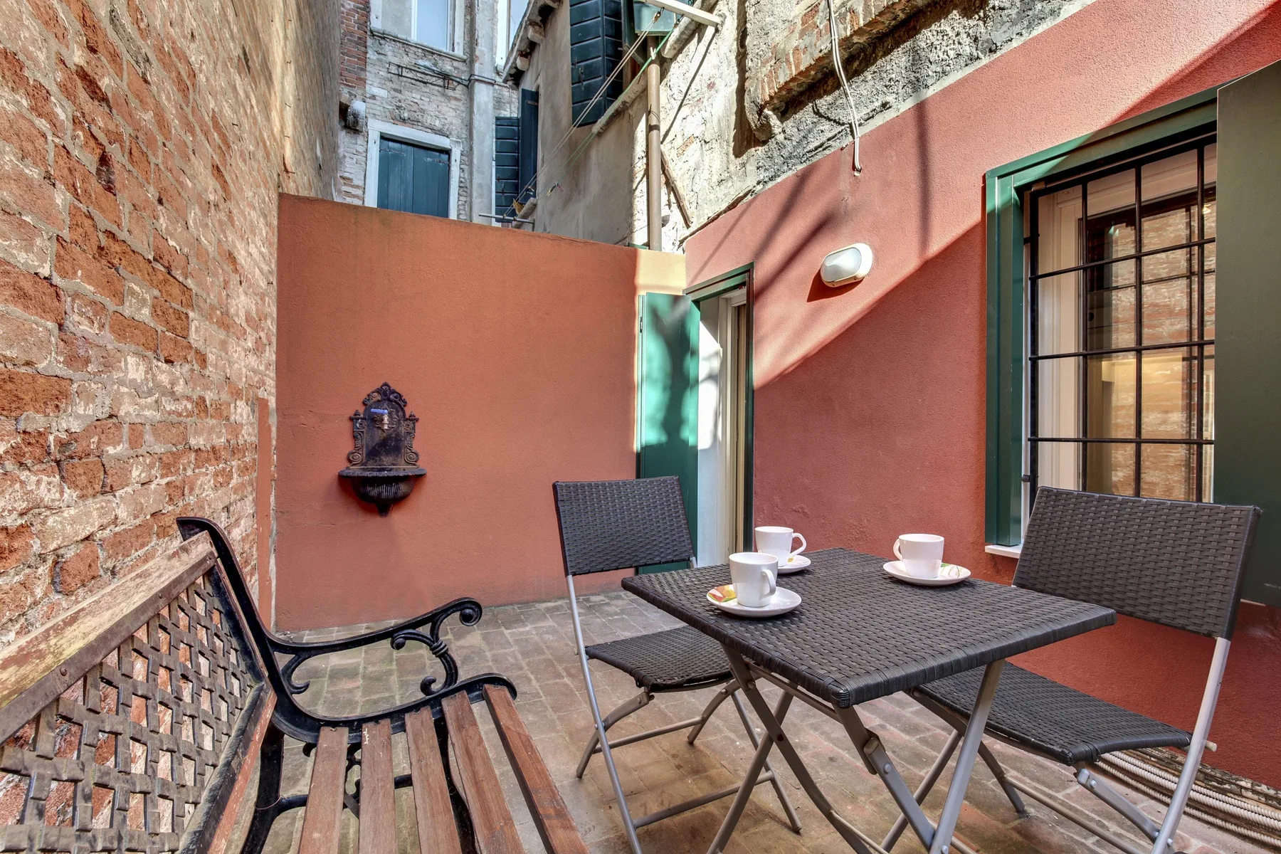 A small outdoor patio has a dining table, chairs, and a wooden bench.