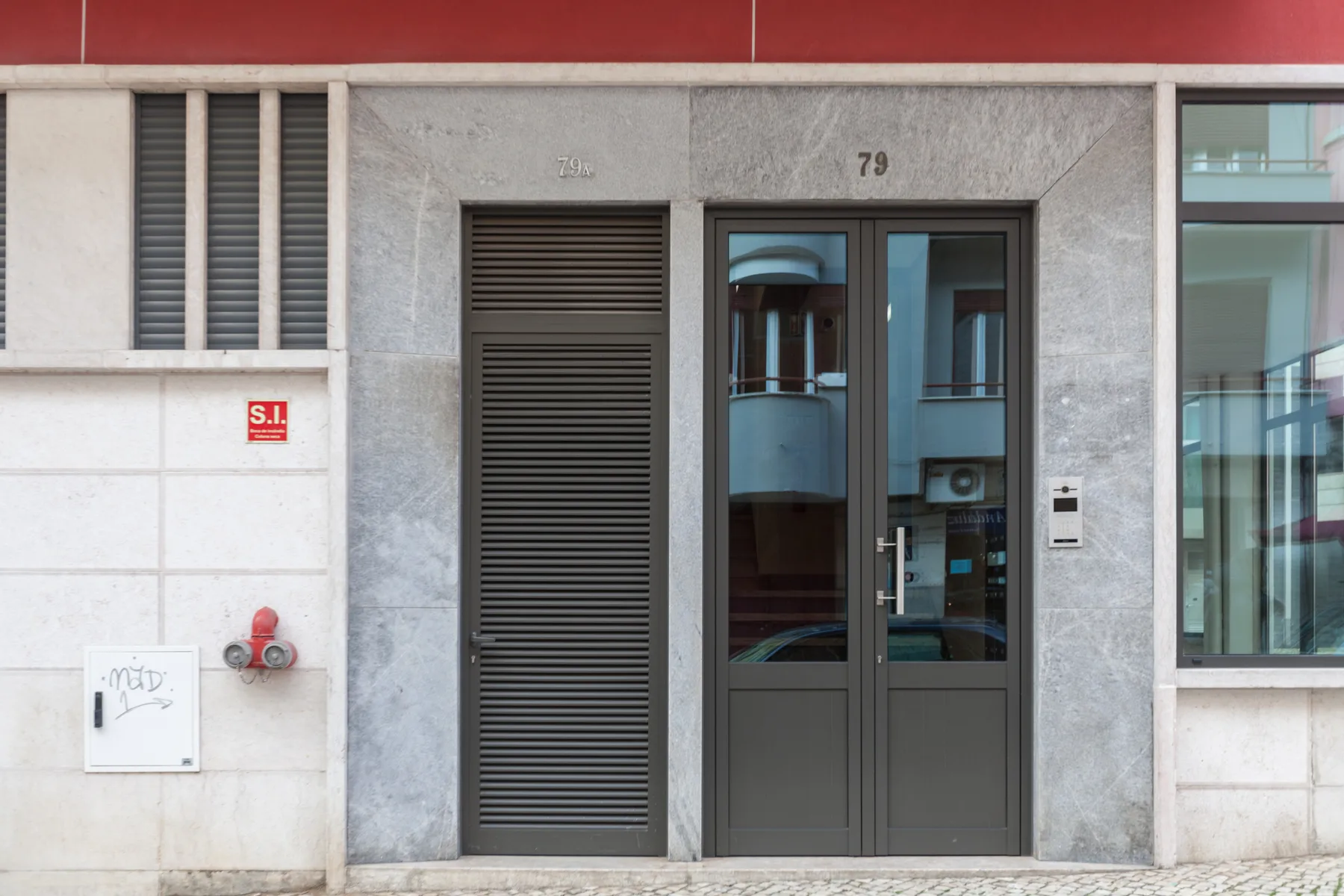 Entrada de edificio con una puerta doble oscura y un panel de lamas.