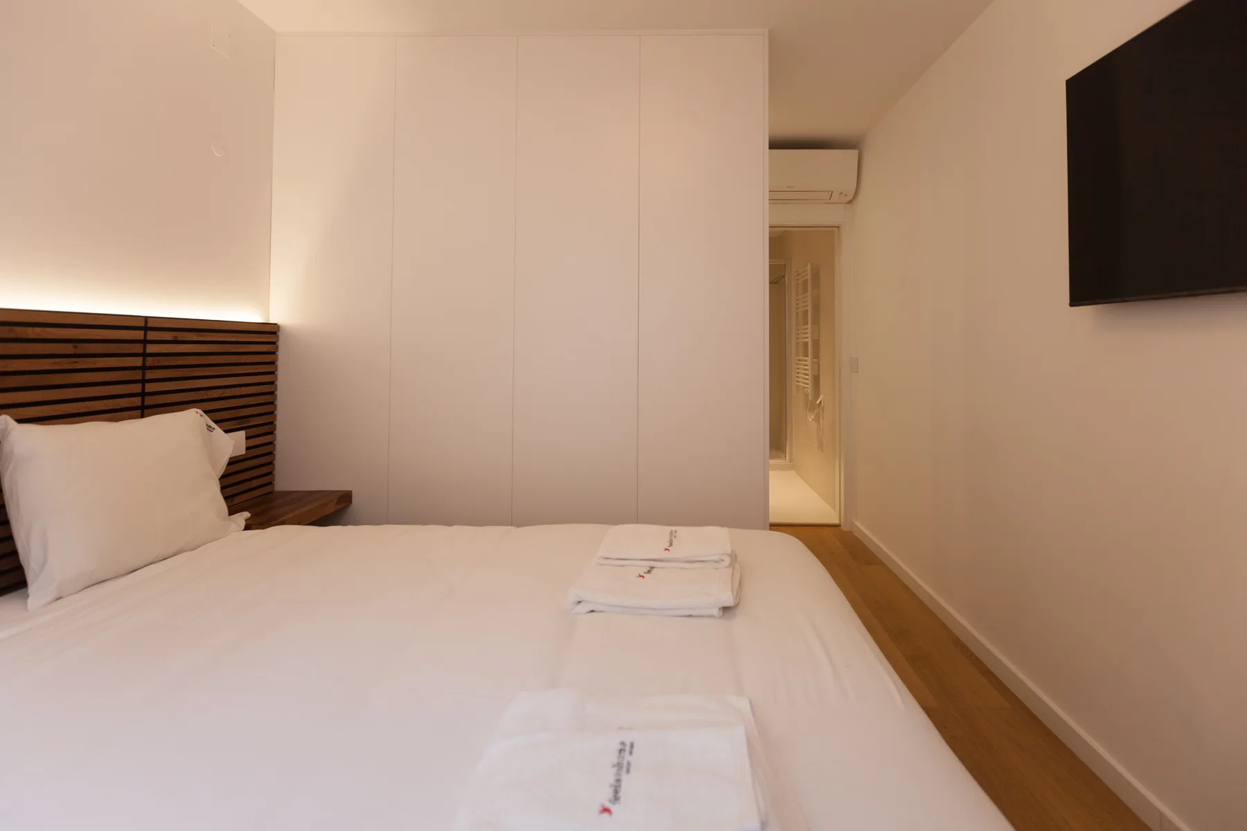 Un dormitorio con una cama bien tendida y un televisor en la pared.