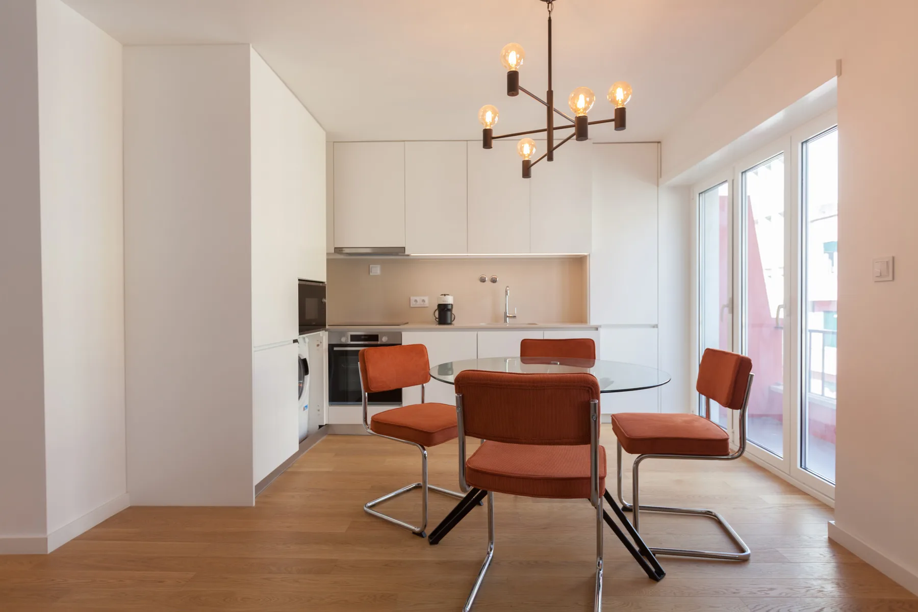 Comedor con mesa y asientos rojos junto a una cocina luminosa.