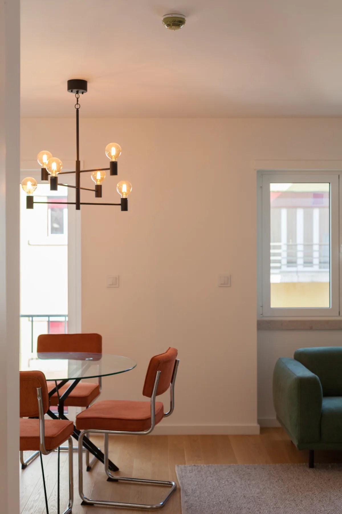 Comedor con mesa de vidrio y asientos junto a una sala de estar.