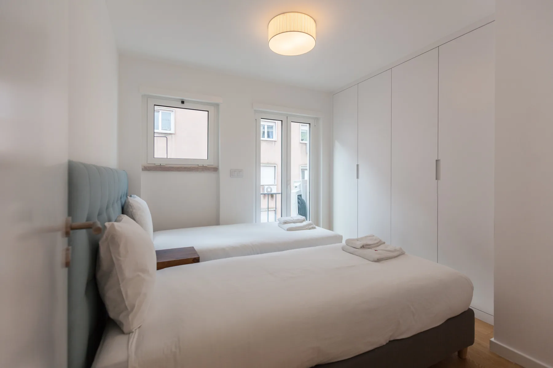 Un dormitorio luminoso con camas, ropa de cama blanca y armarios empotrados.