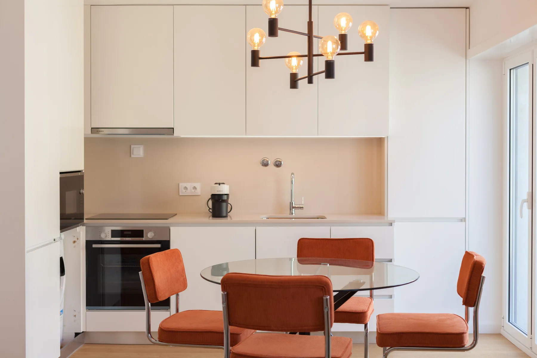 Una cocina moderna con una mesa de comedor y asientos naranjas junto a una ventana amplia.