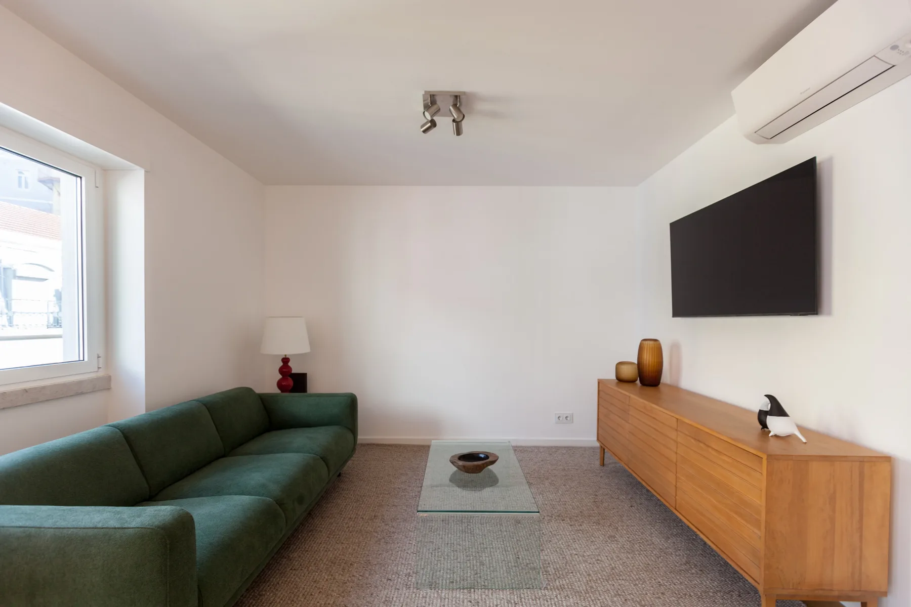 Sala de estar con asientos verdes, un televisor y un mueble de madera.