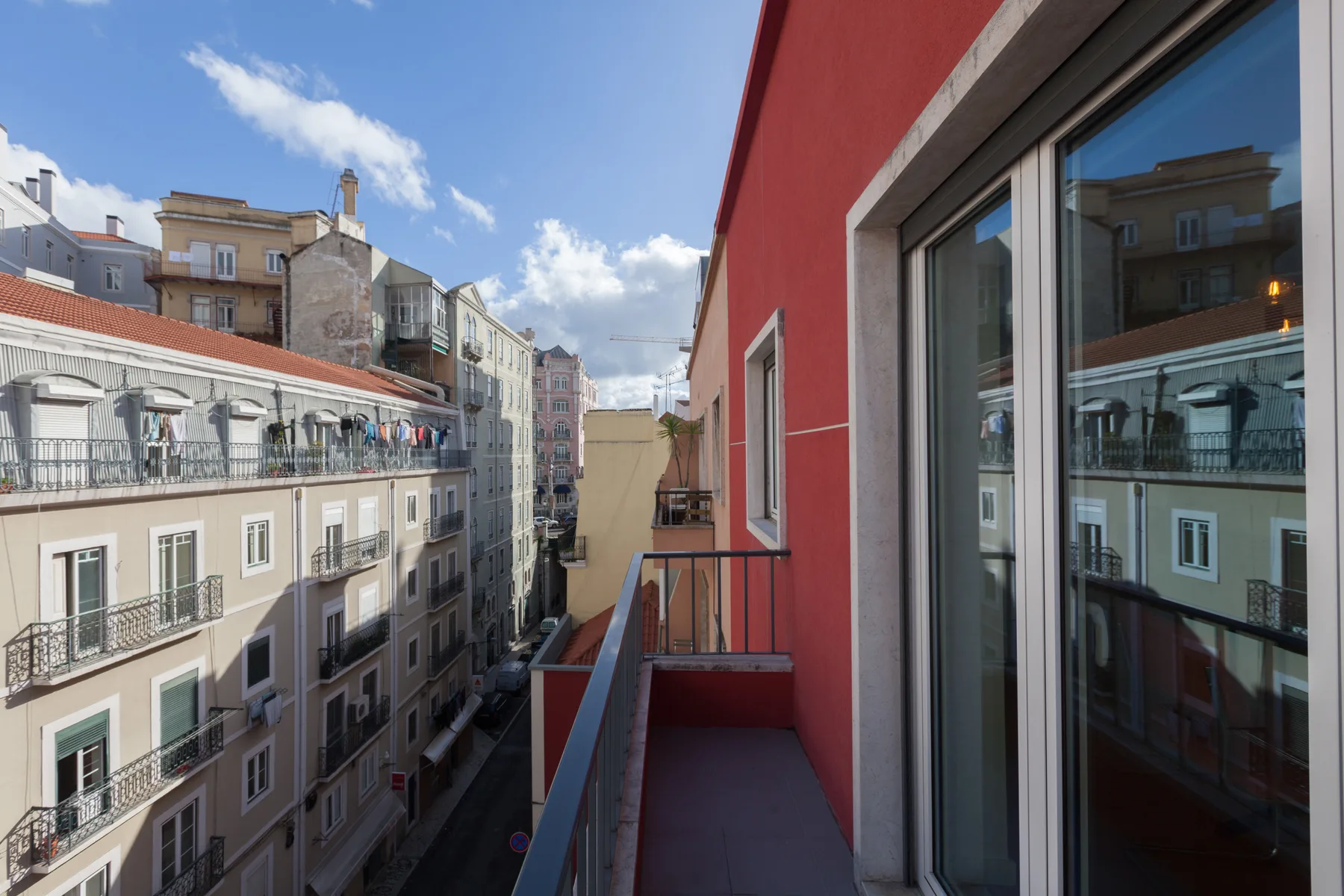 Un balcón estrecho da a una calle urbana con edificios de apartamentos.