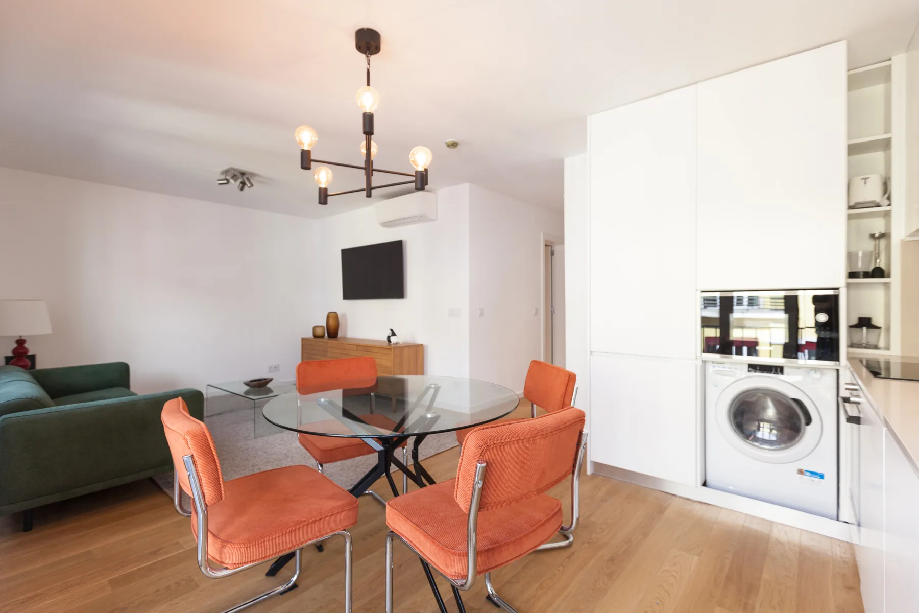 Una luminosa sala de estar y comedor con asientos naranjas y una mesa de cristal.