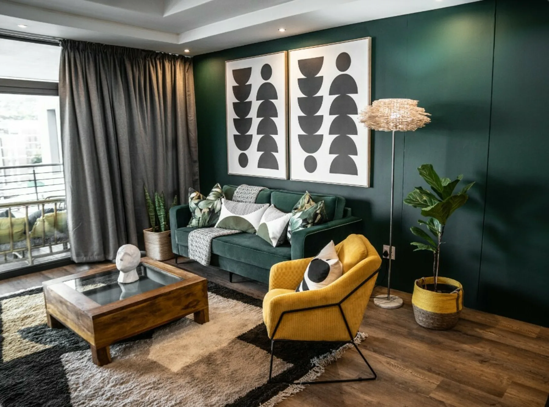 A living room with green seating, a yellow chair, and framed wall art.