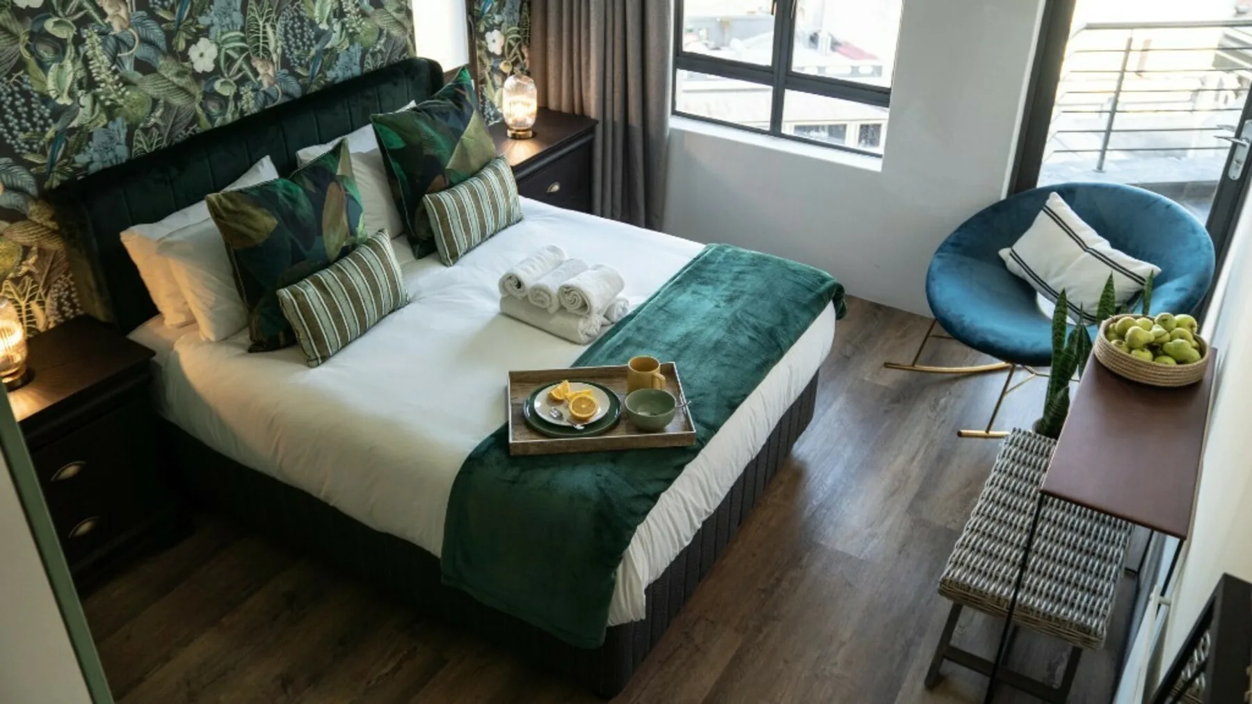 A bedroom with a neatly made bed and a blue chair beside the windows.