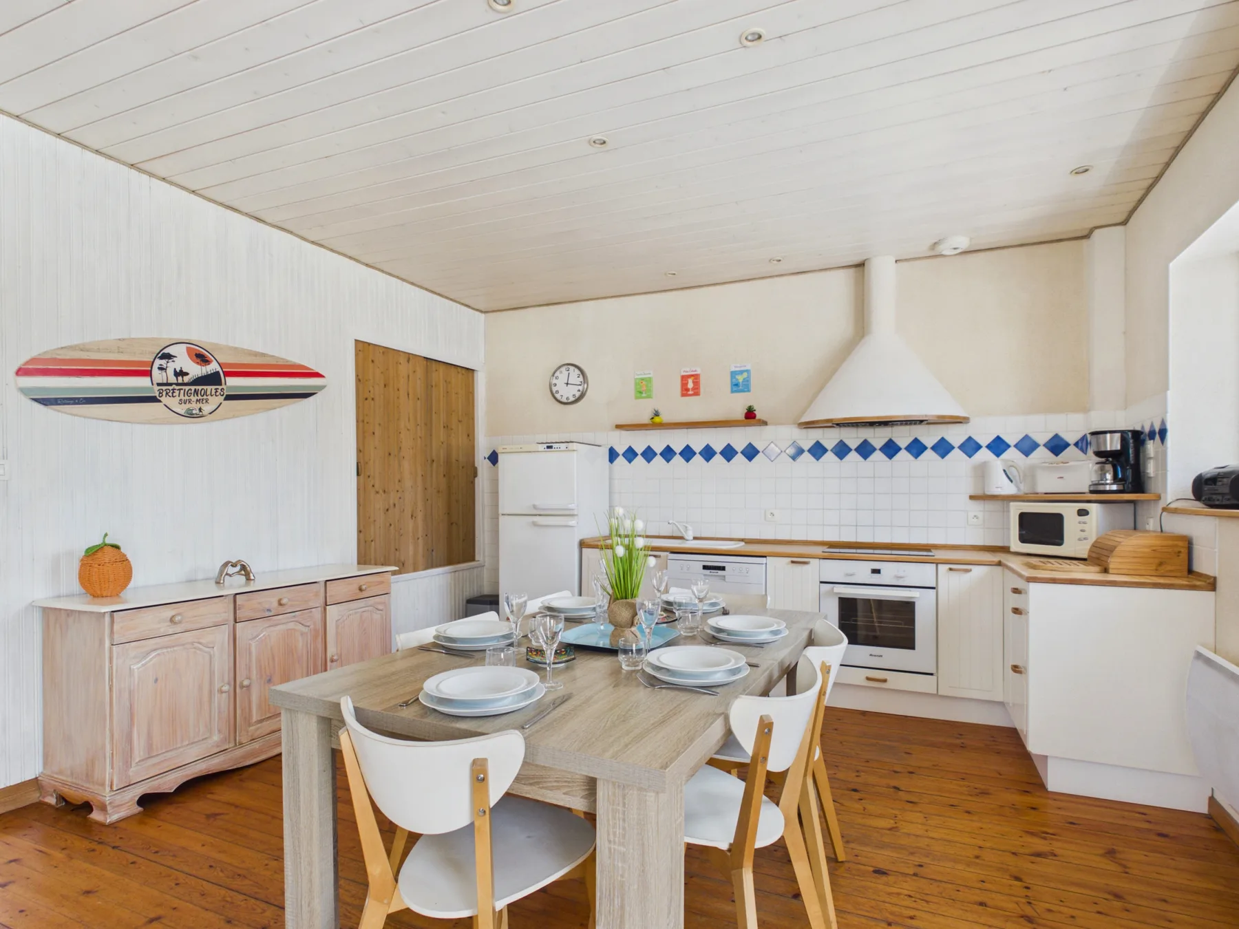 A dining table sits in a bright kitchen with white cabinets and a wooden floor.