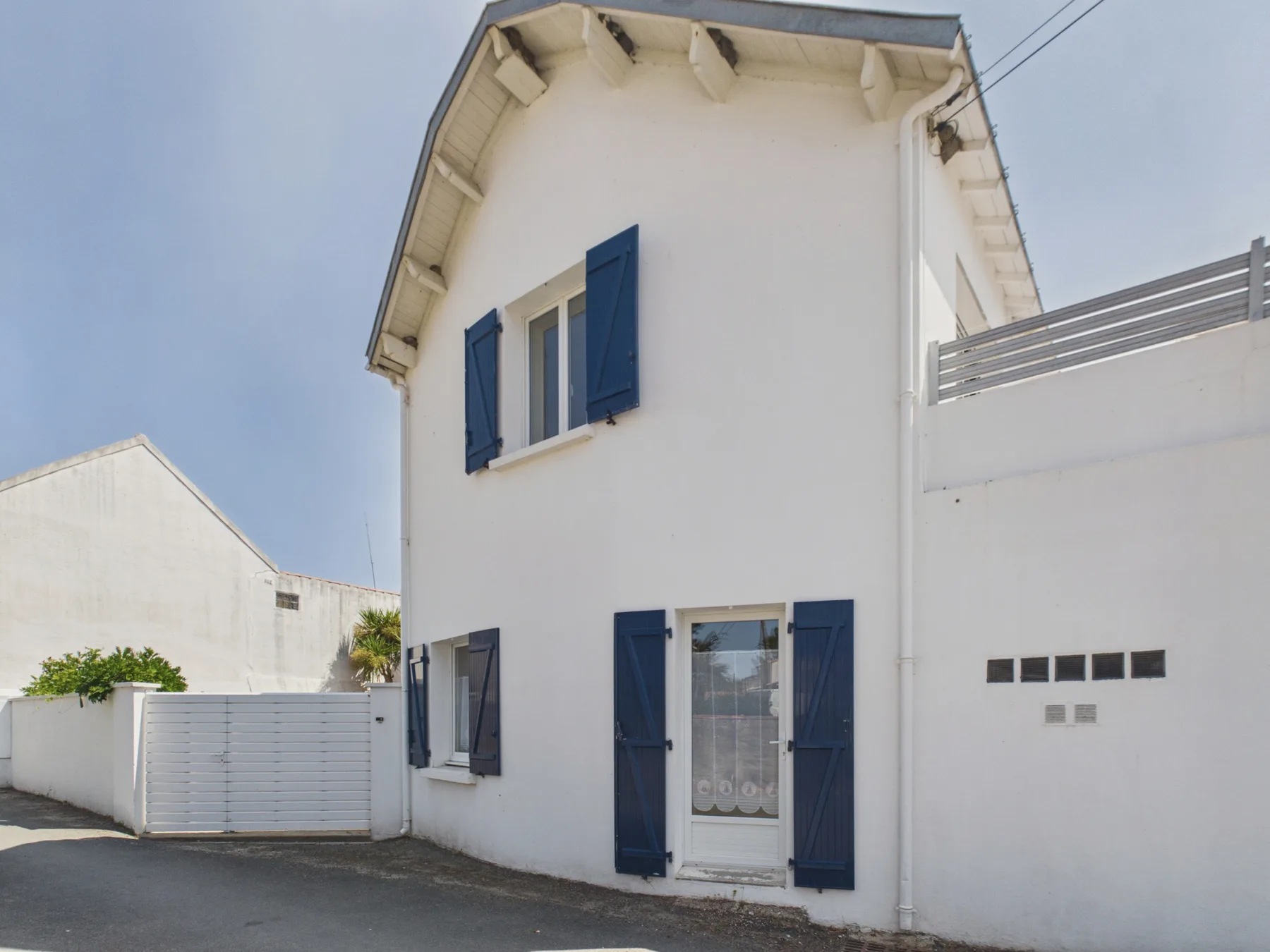 A white two-story house with blue shutters and a paved driveway.