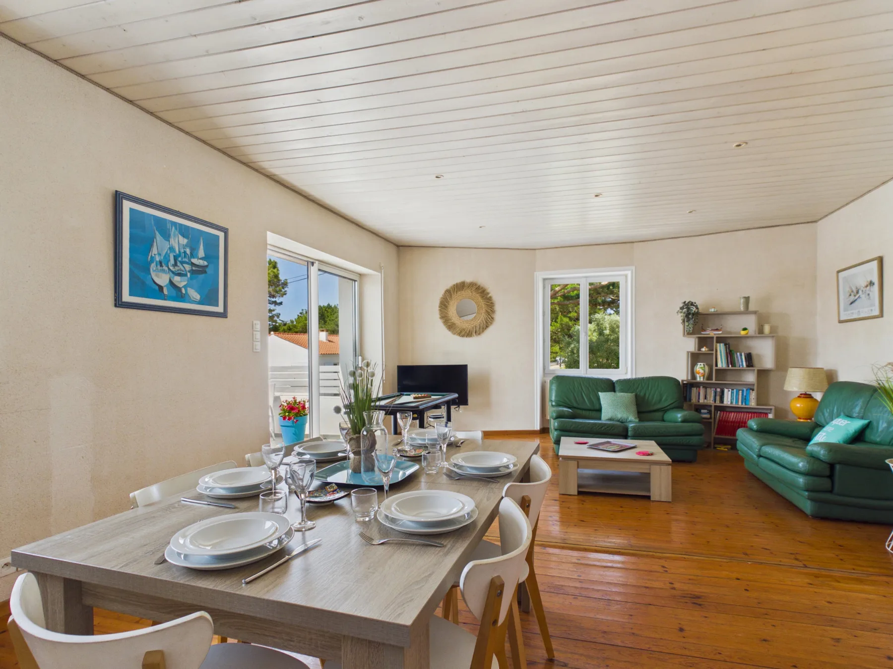 A bright living and dining room with a set table and green seating.