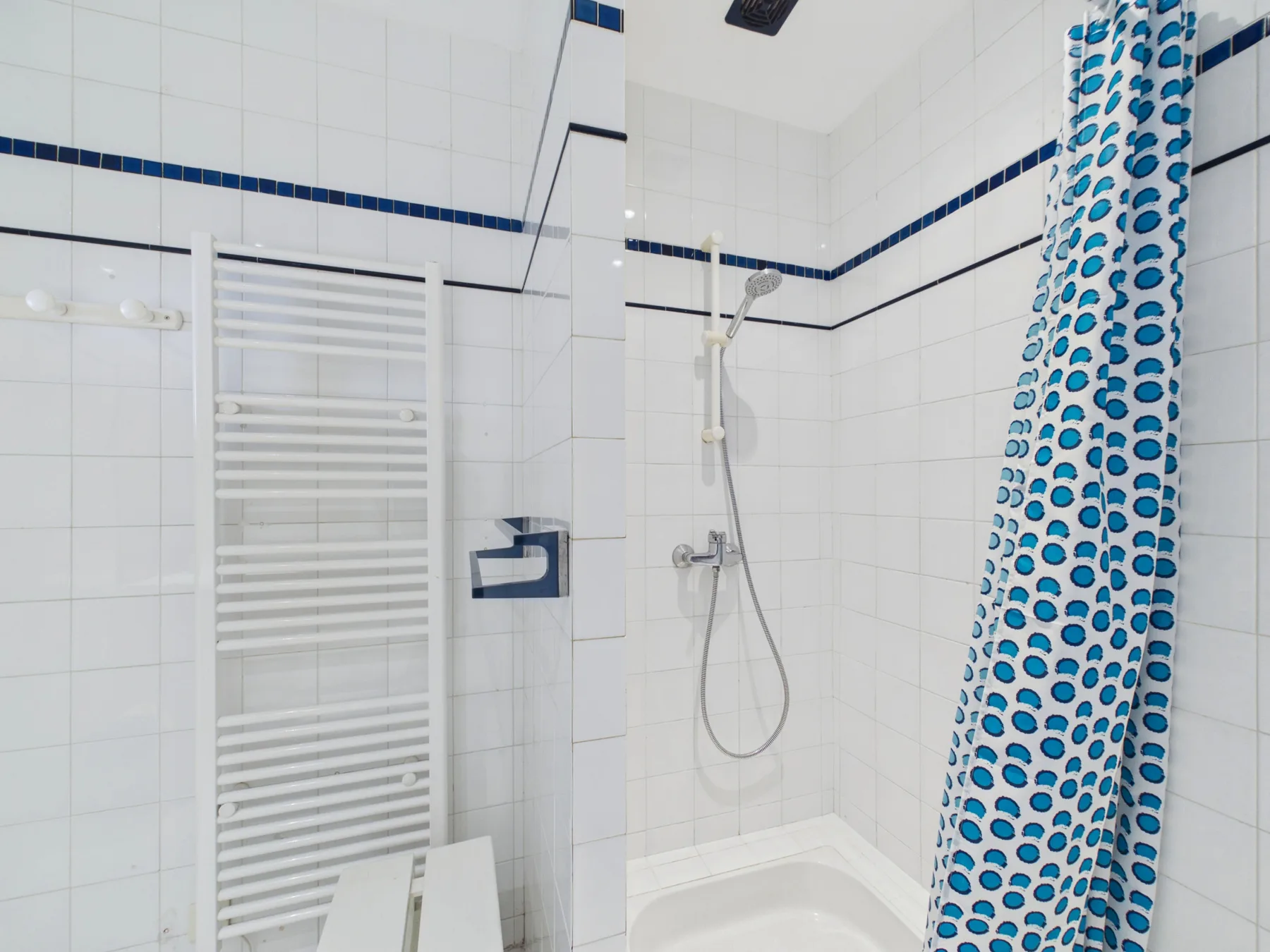 A tiled bathroom with a shower and patterned curtain.