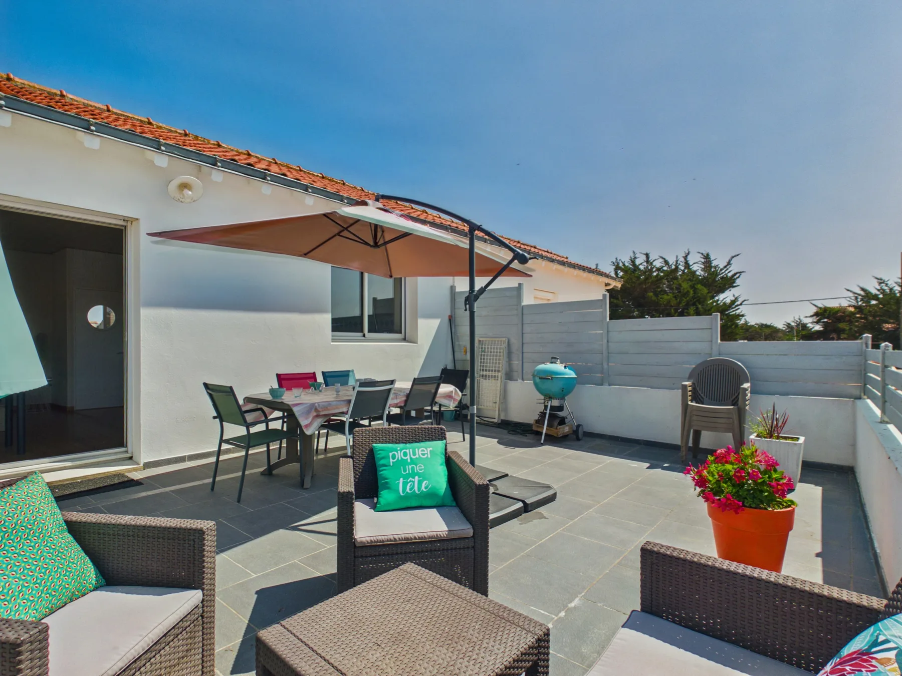 A sunny tiled patio with outdoor seating and a large shade umbrella.
