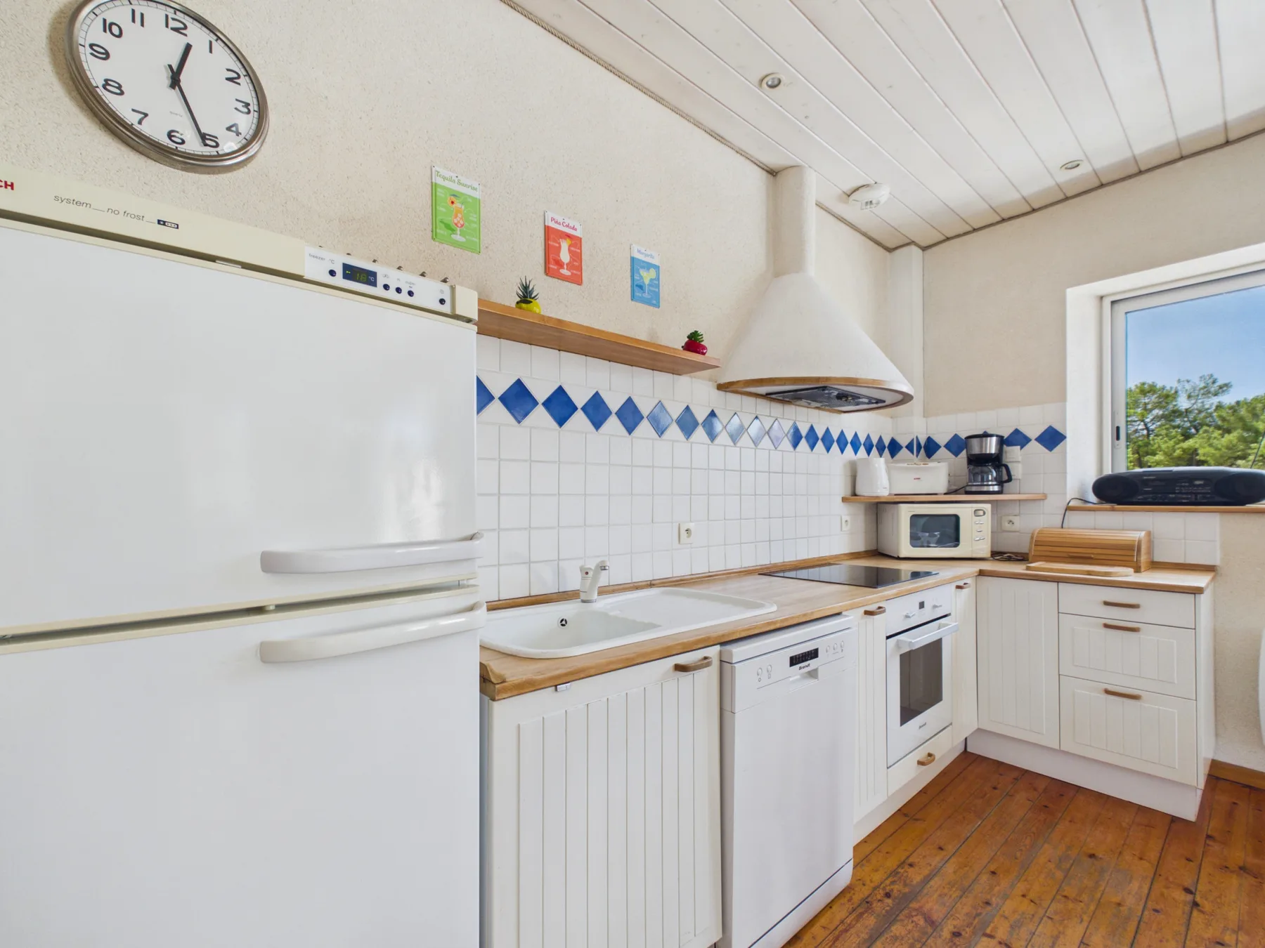 A bright kitchen with white cabinetry, tiled walls, and a window.