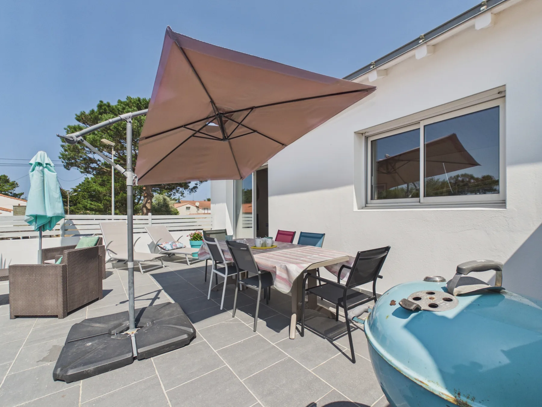 A sunny outdoor patio with a dining table, seating, and a large umbrella.