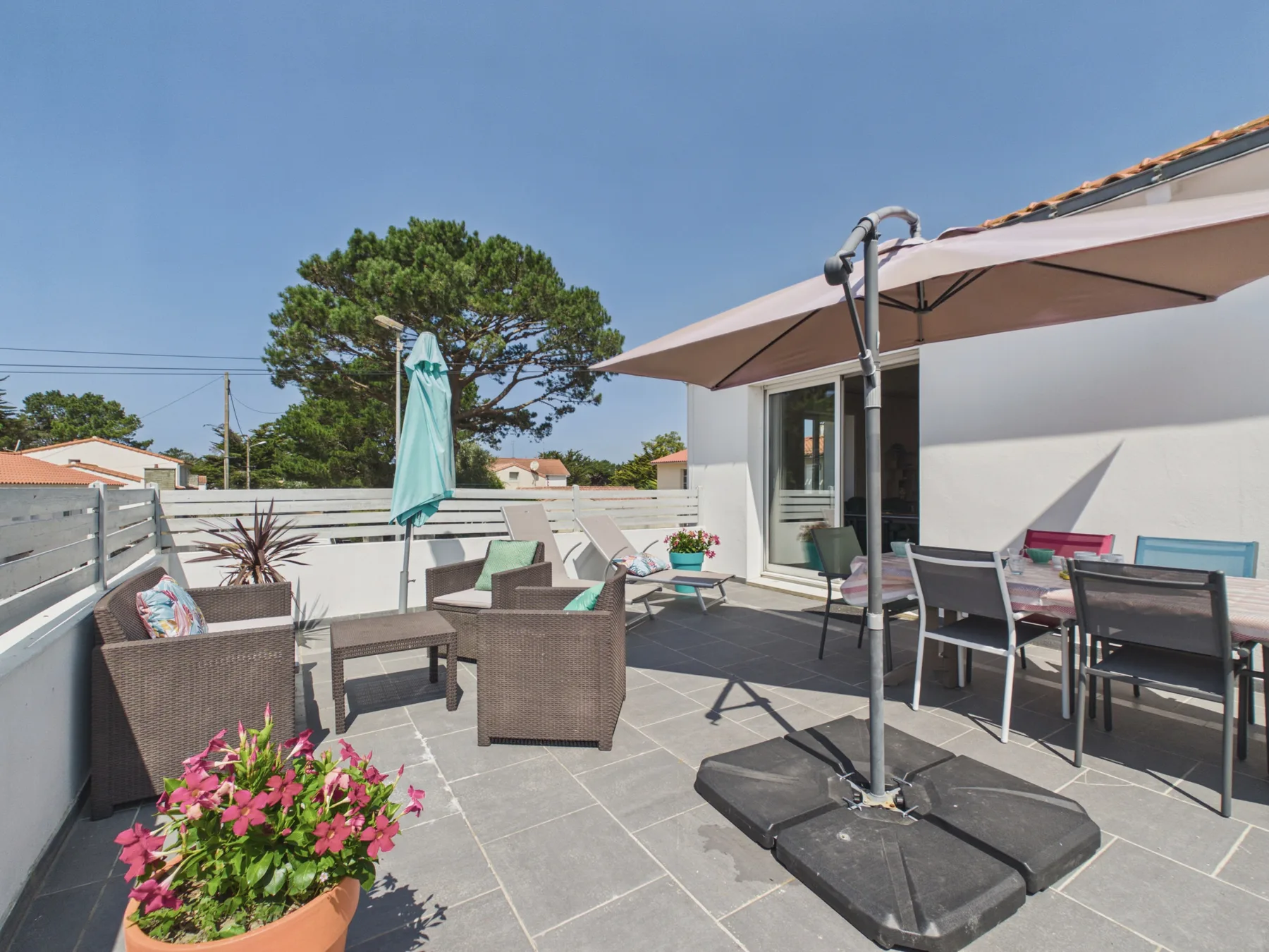 A sunny patio with outdoor seating, a large umbrella, and potted flowers.