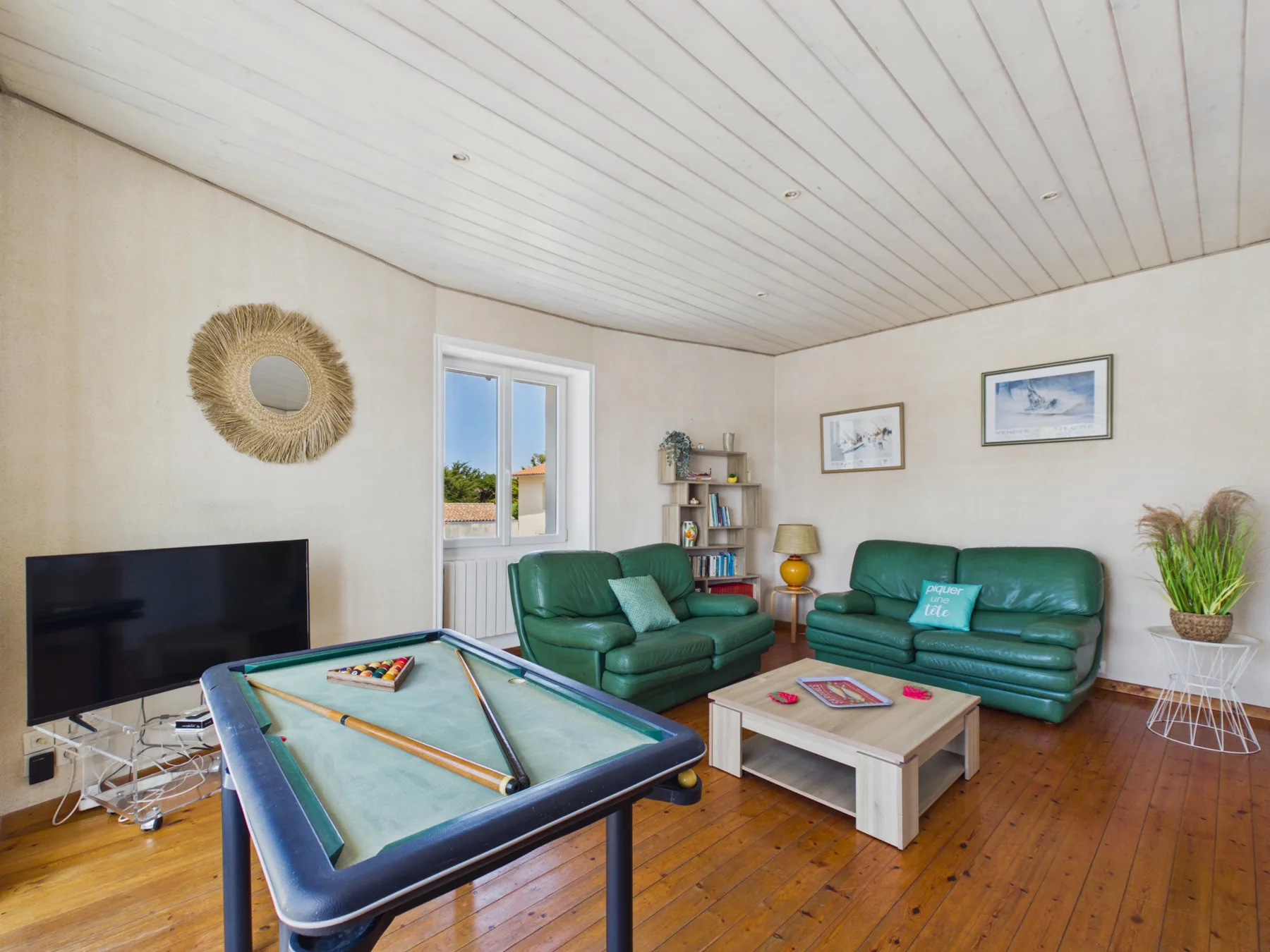 A living room with green seating, a television, and a pool table.