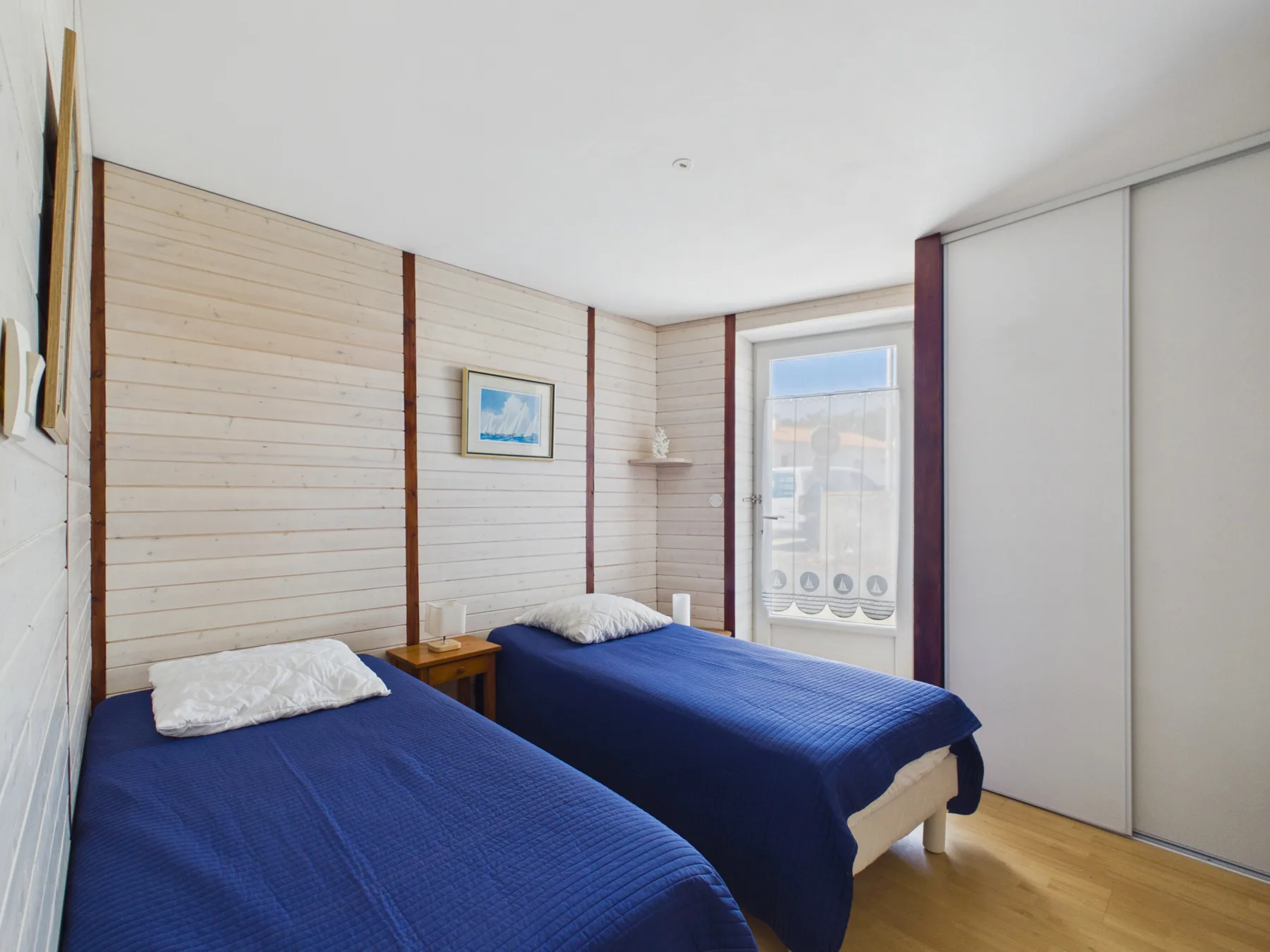A bedroom with two beds covered in blue bedding and a window.