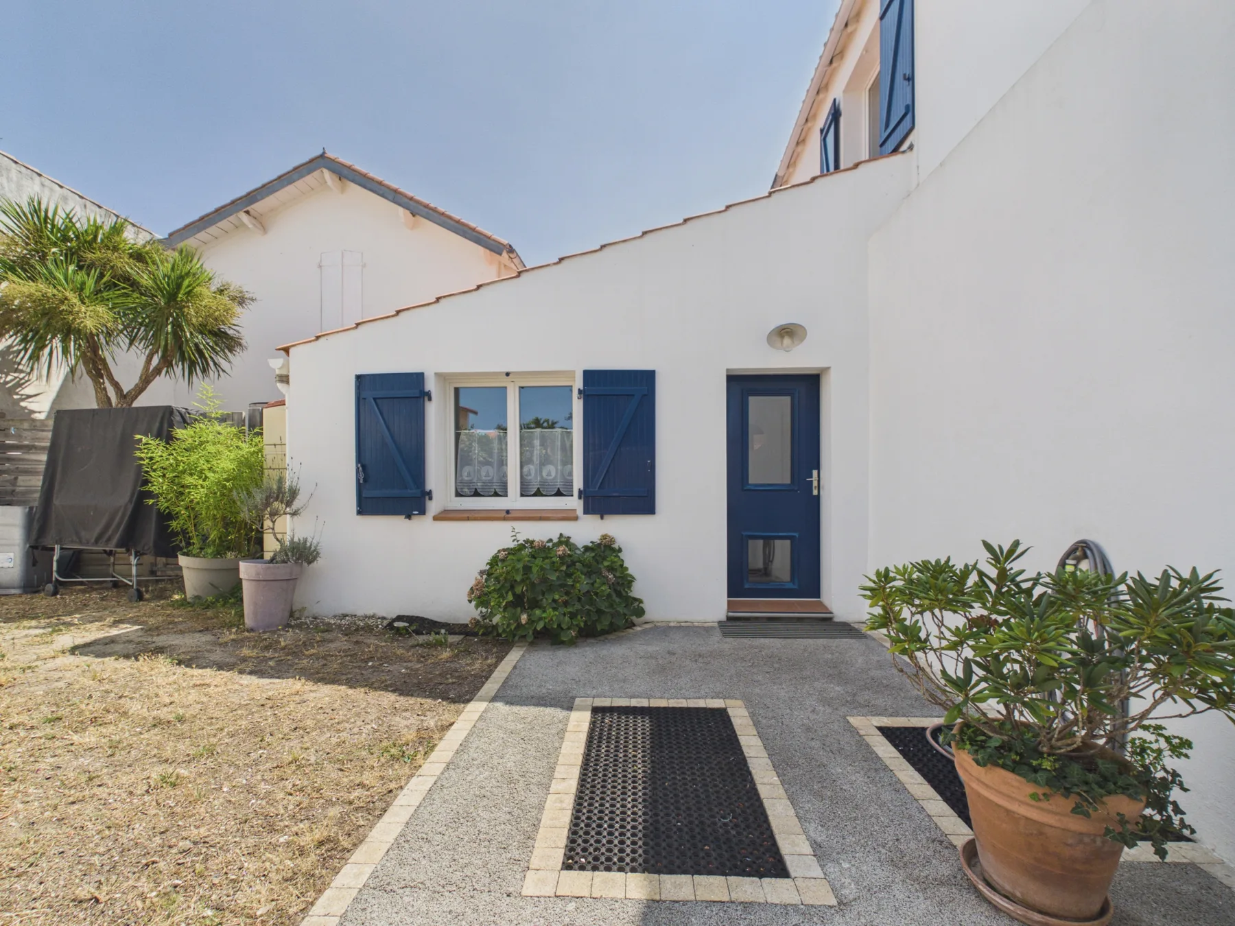 White house entrance with blue shutters, a blue door, and potted plants.