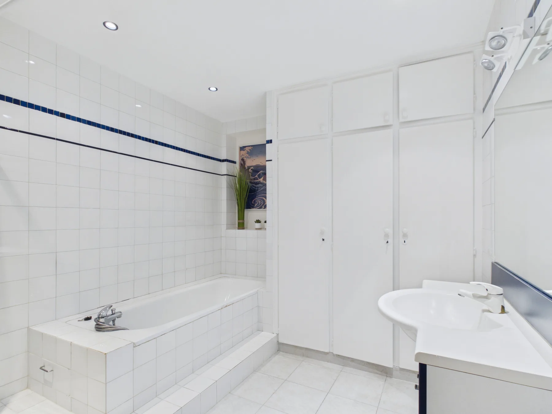A tiled bathroom with a bathtub, white cabinets, and a sink.