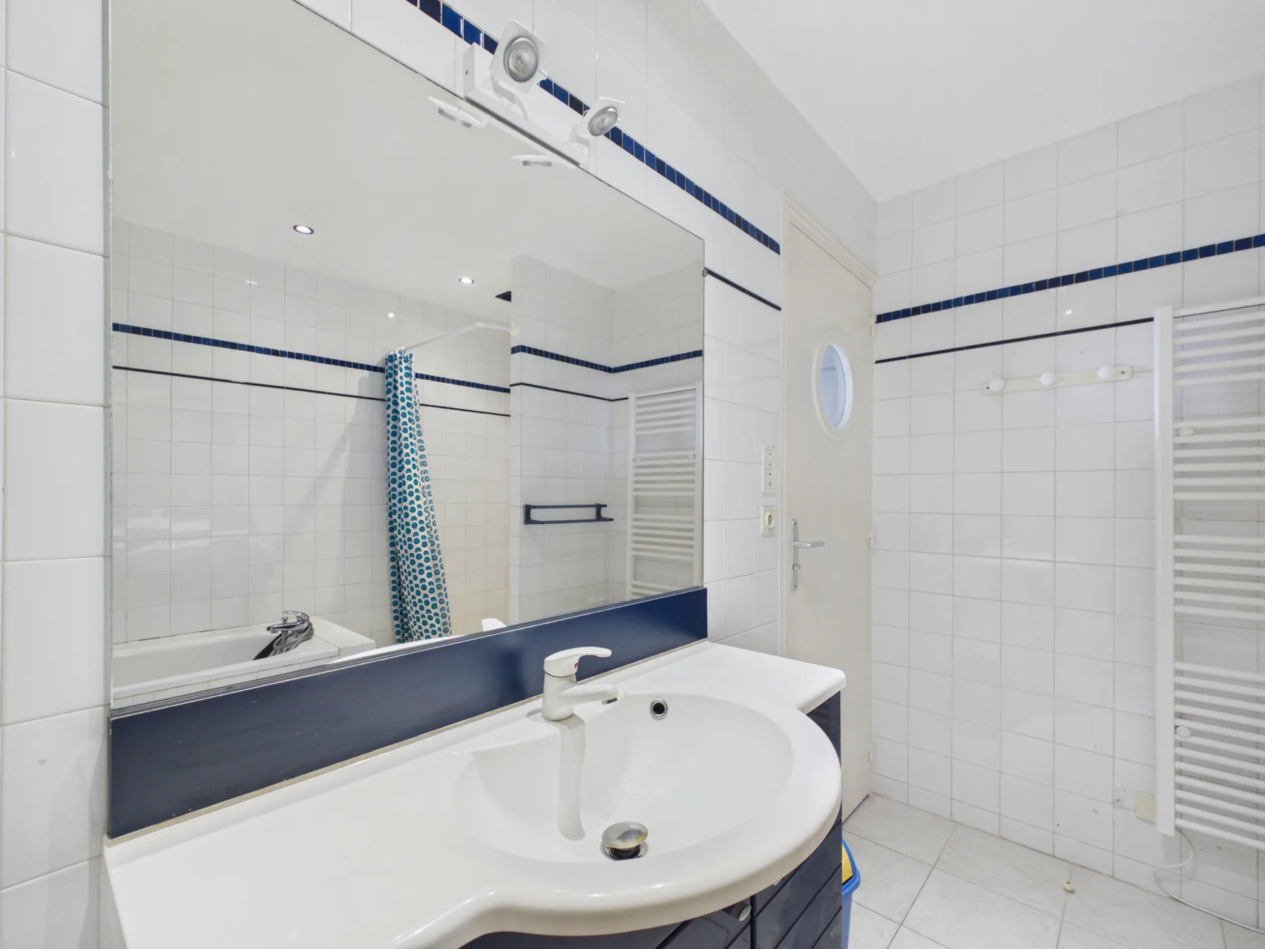 A tiled bathroom has a sink beneath a large mirror.