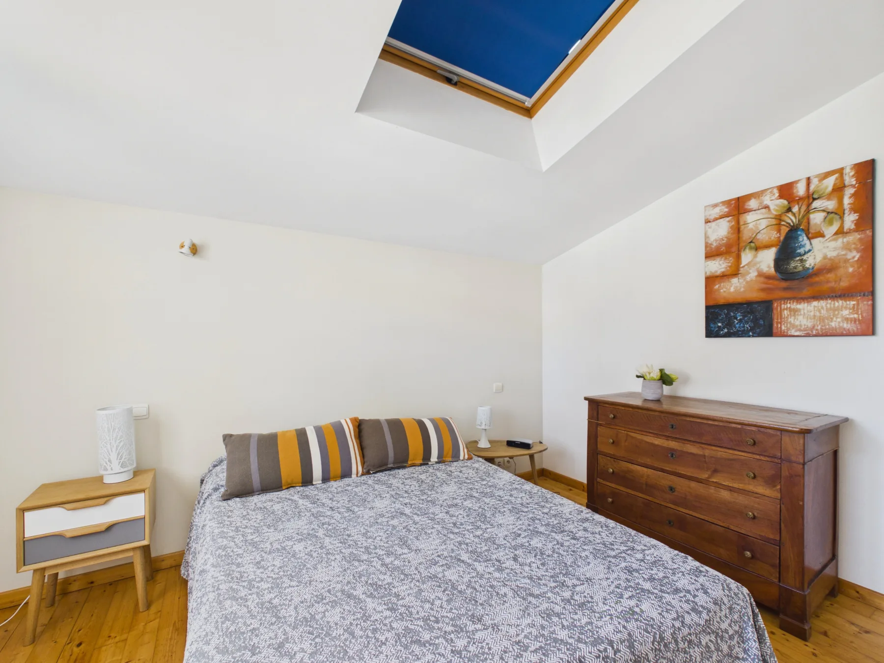 A bedroom with a bed, wooden dresser, and skylight.