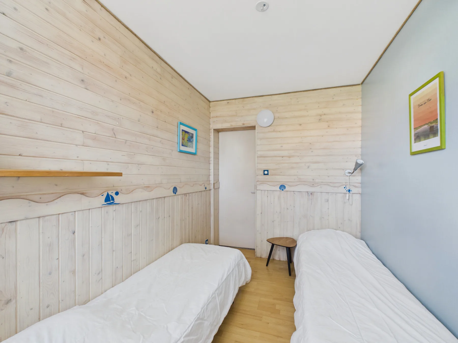 A bedroom with two single beds and light wood-paneled walls.