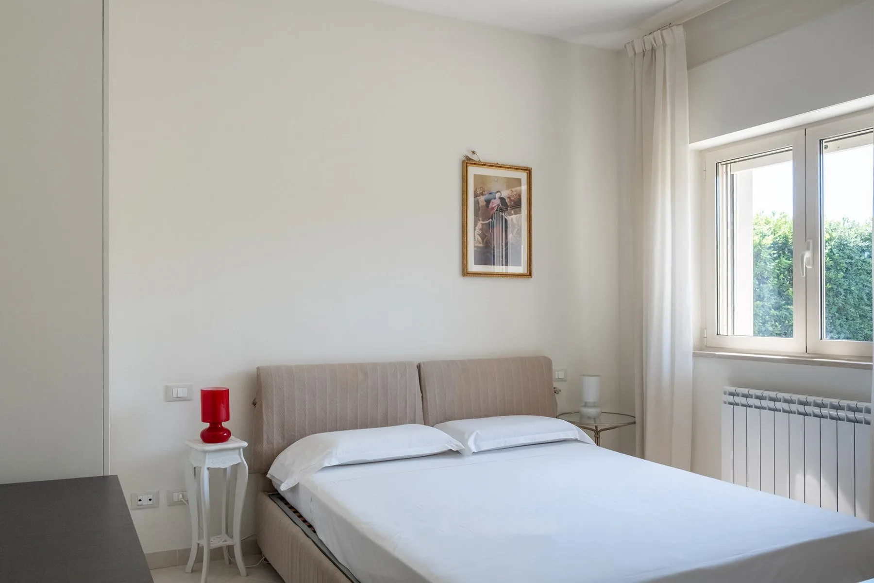 A bright bedroom with a double bed beneath a framed picture.