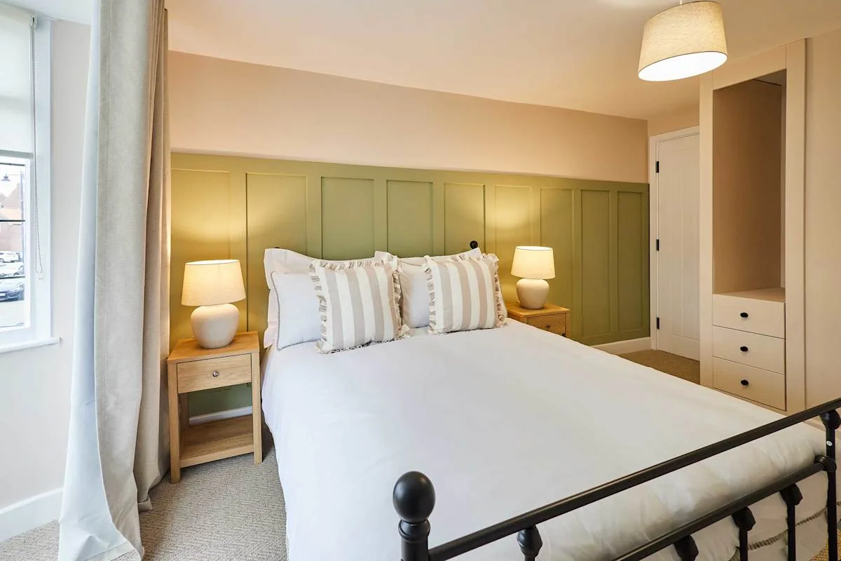 Dormitorio con una cama grande y una pared verde con paneles.