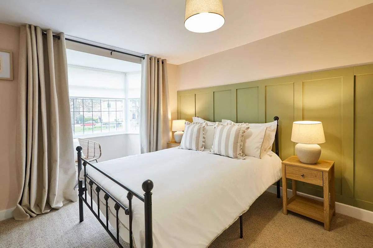 Dormitorio con cama, pared verde con paneles y ventana con cortinas.
