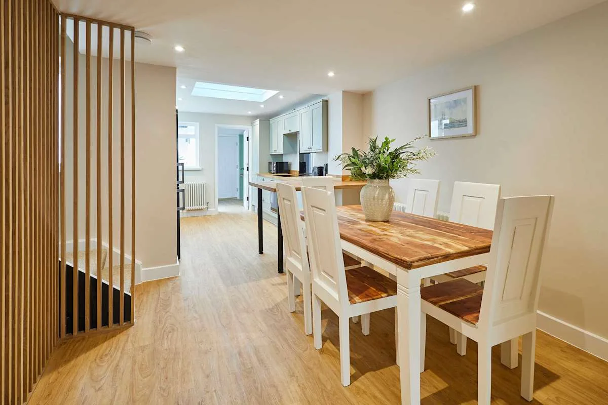 Comedor con una mesa de madera y sillas blancas junto a una cocina abierta.