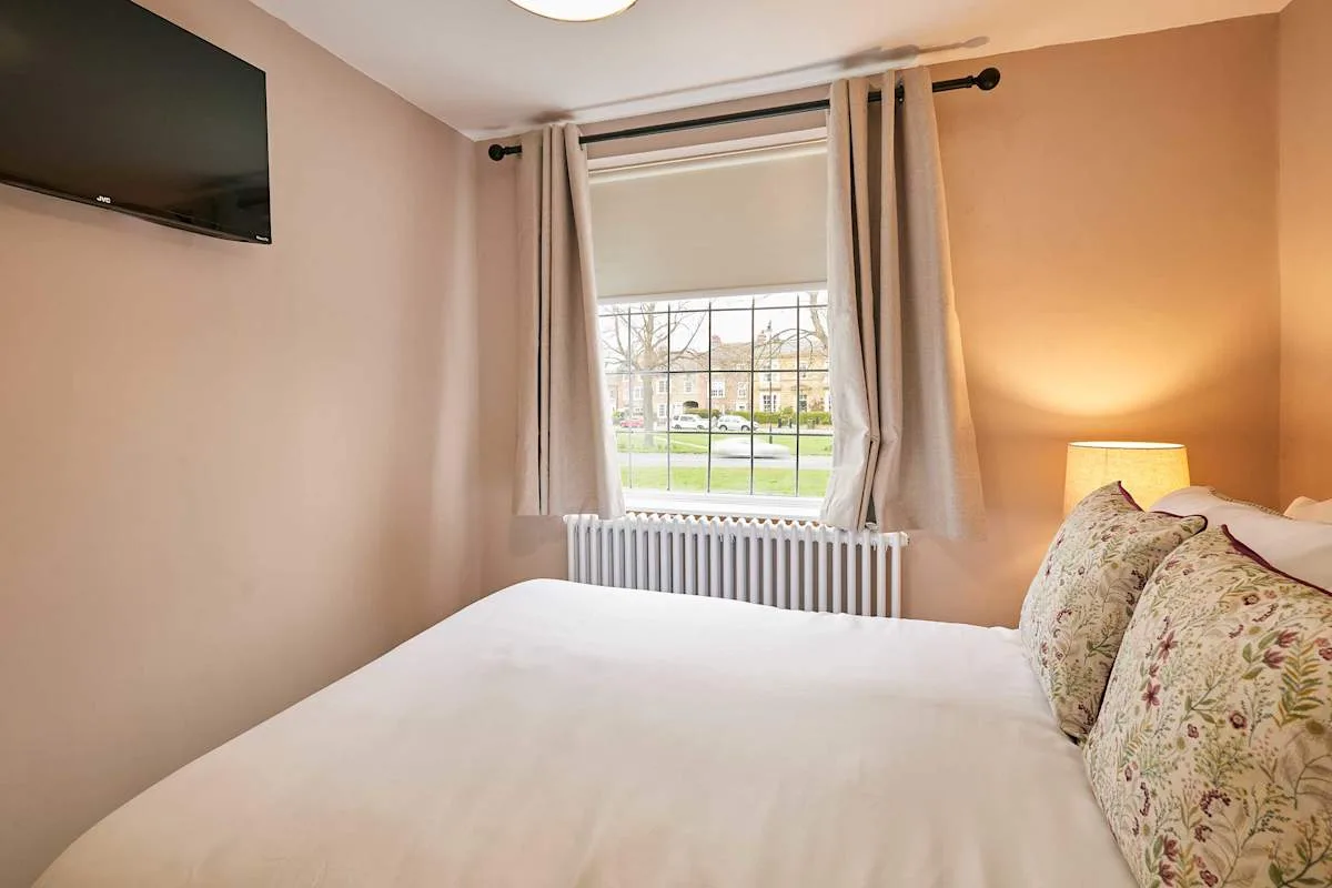 Un dormitorio con una cama, cojines florales y una ventana con cortinas.