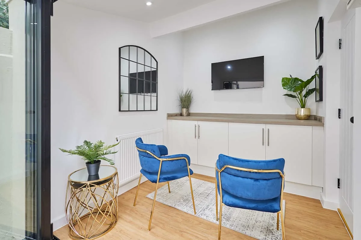 Una luminosa zona de estar con asientos azules, un televisor en la pared y armarios empotrados.