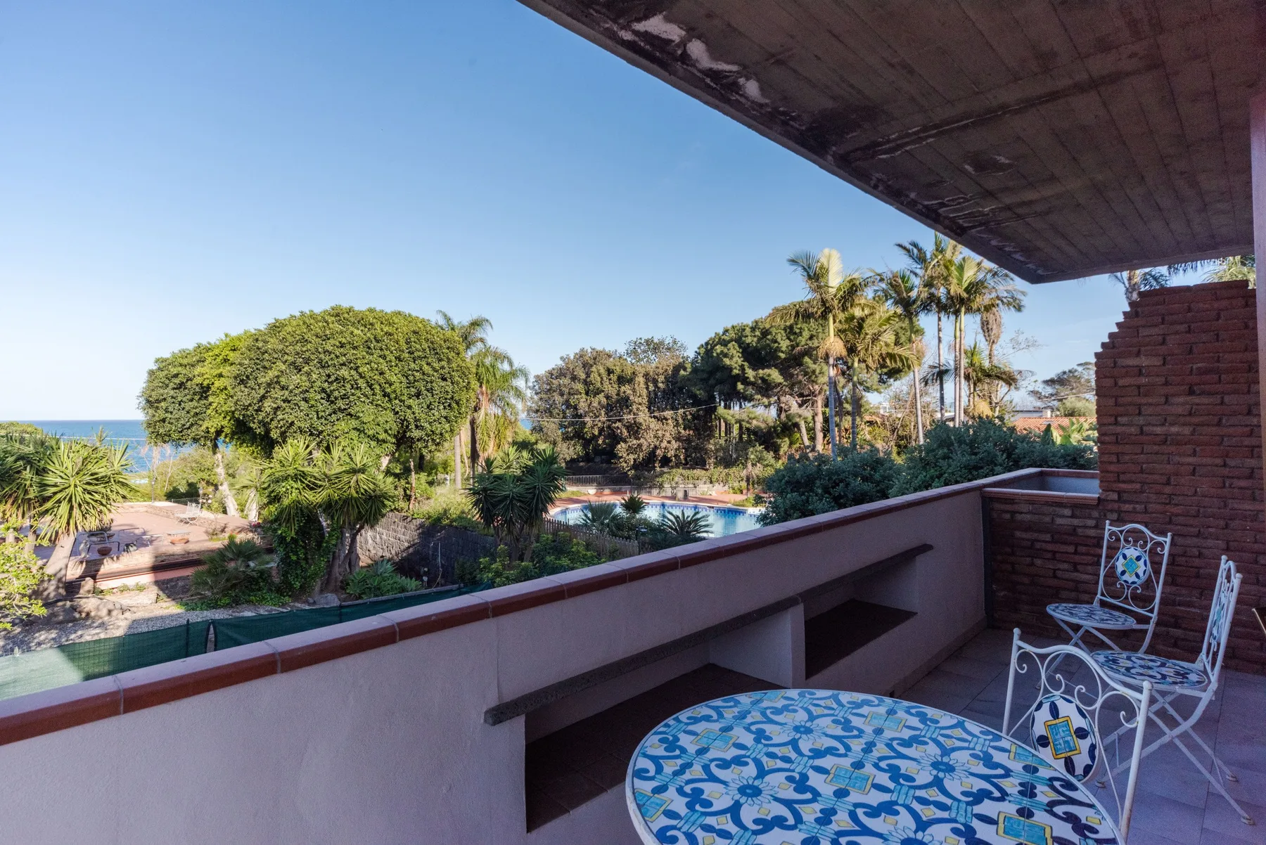 Una terraza cubierta da a un jardín con palmeras y una piscina.