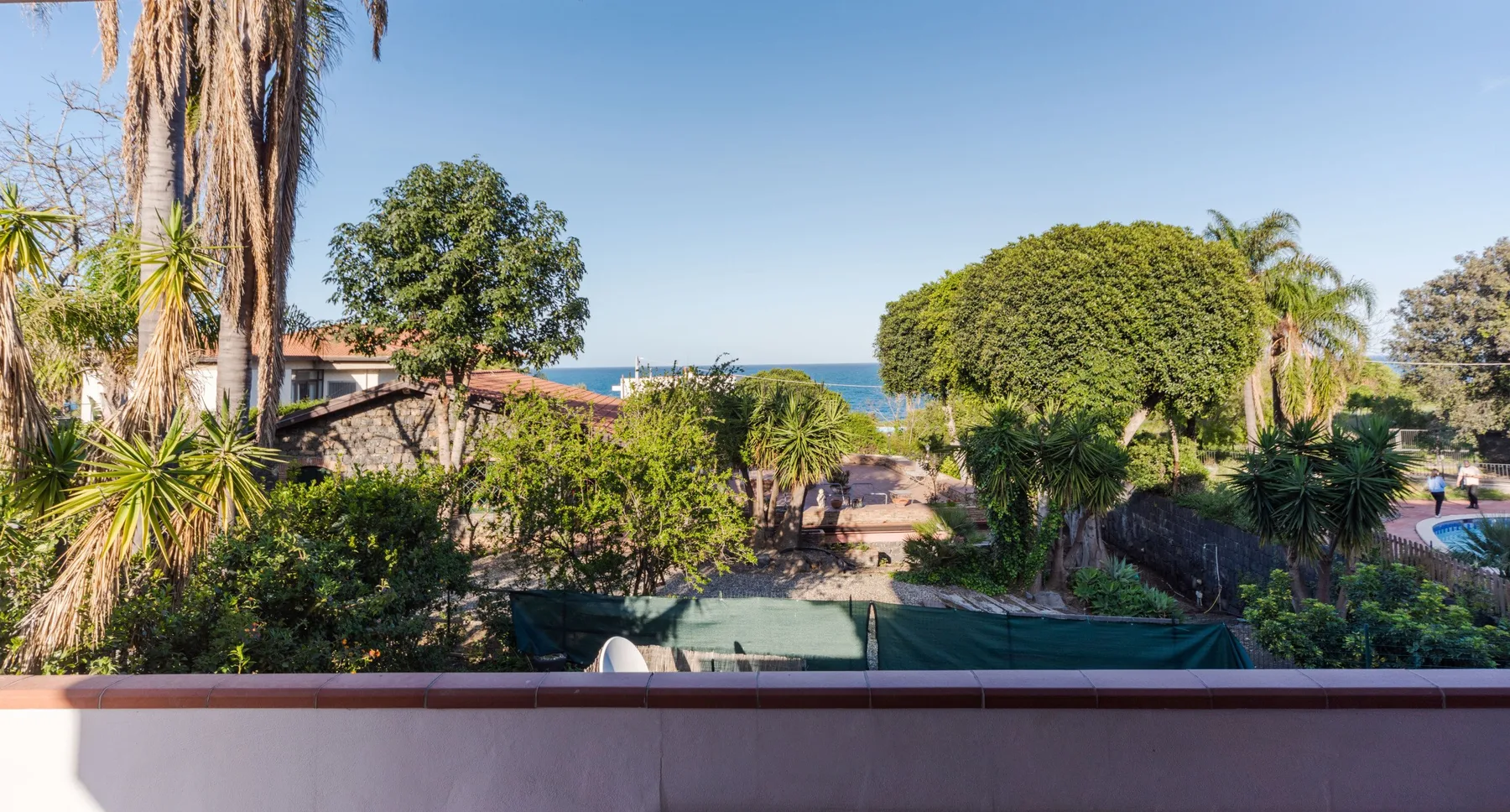 Un jardín con árboles y arbustos tiene vistas al mar.