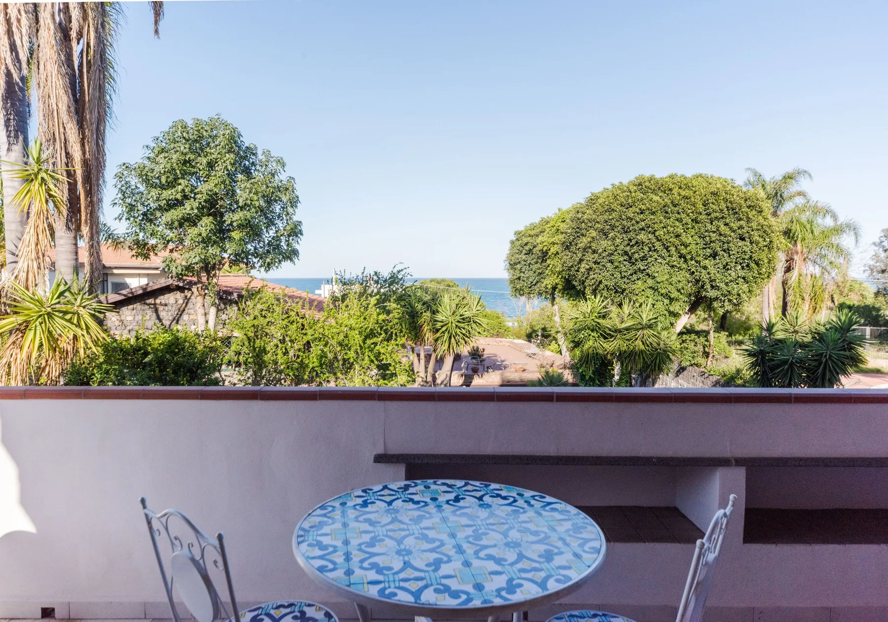 Un patio exterior tiene una mesa redonda estampada con vistas a un jardín frondoso.